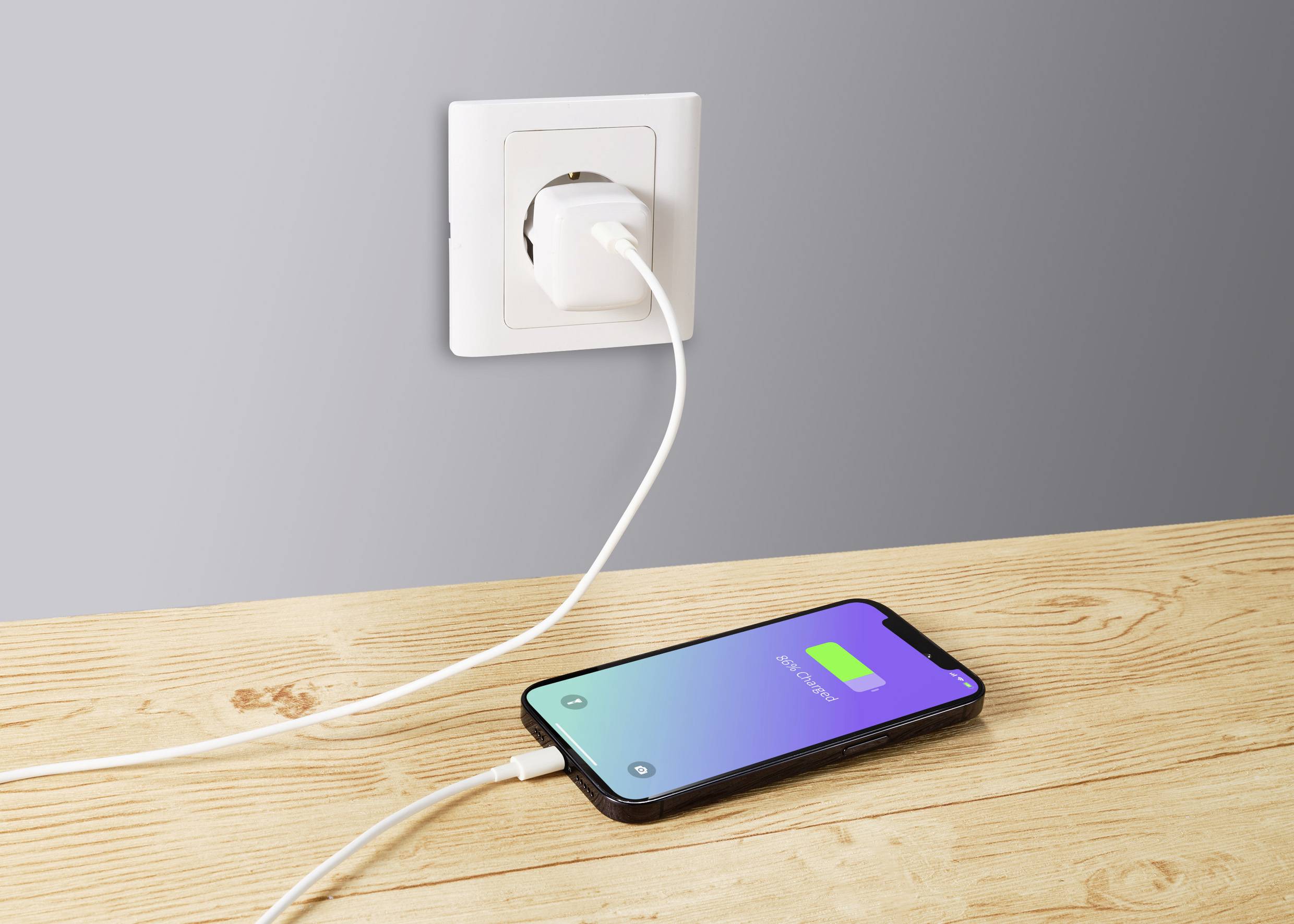 Mobilní telefon leží na dřevěném stole a nabíjí se pomocí kabelu zapojeného do elektrické zásuvky. Obrazovka ukazuje stav nabití 80%.