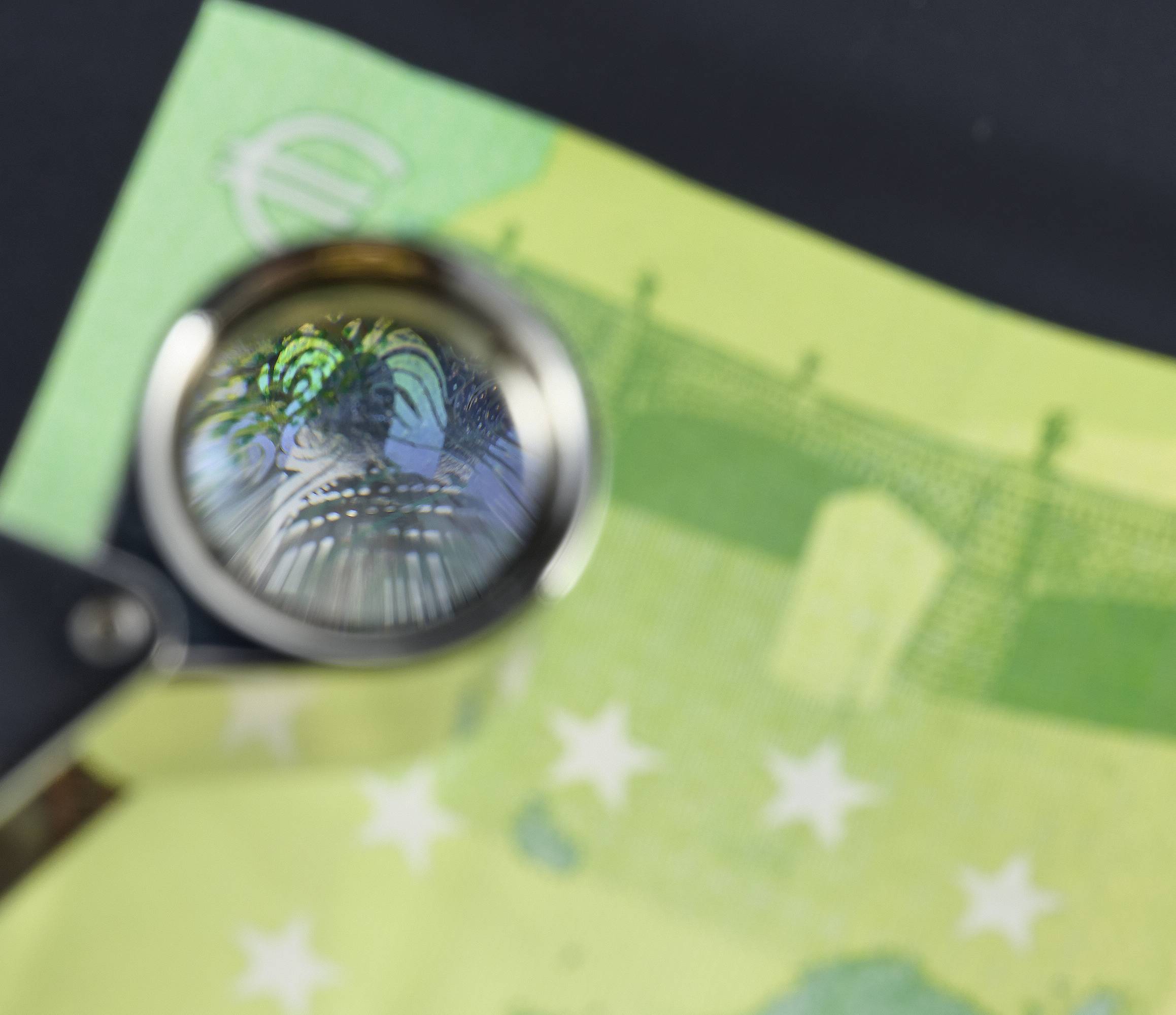 Lupa zvětšuje bezpečnostní prvky na eurobankovce. Hlavním charakteristickým rysem je barevné hologram bankovky.