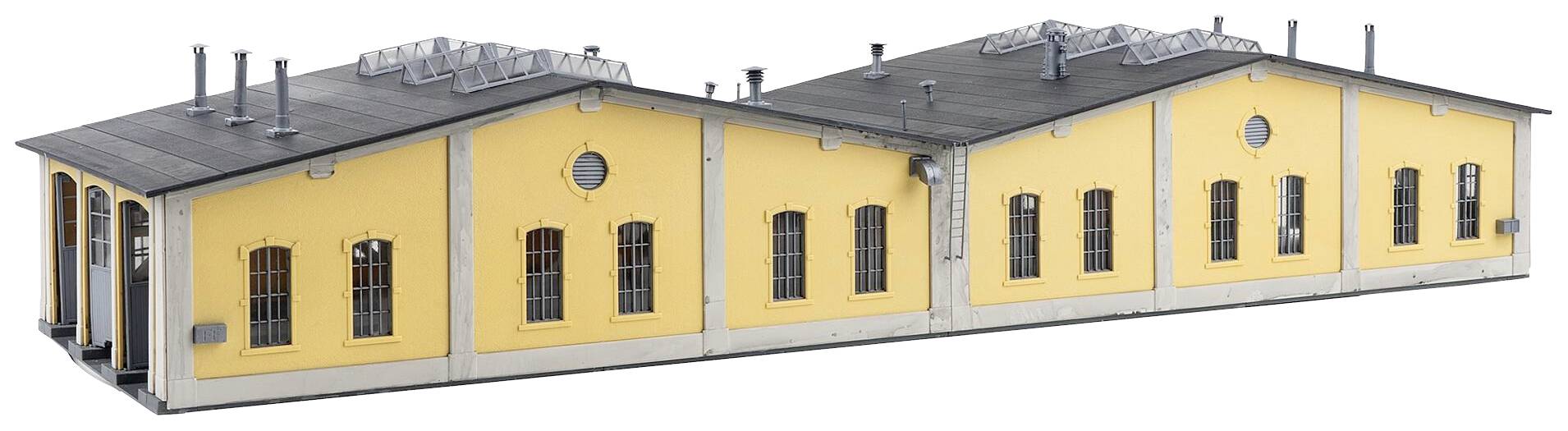 Žlutá cihlová budova s šedými střechami a několika okny; průmyslová architektura s větracími potrubími na střeše.
