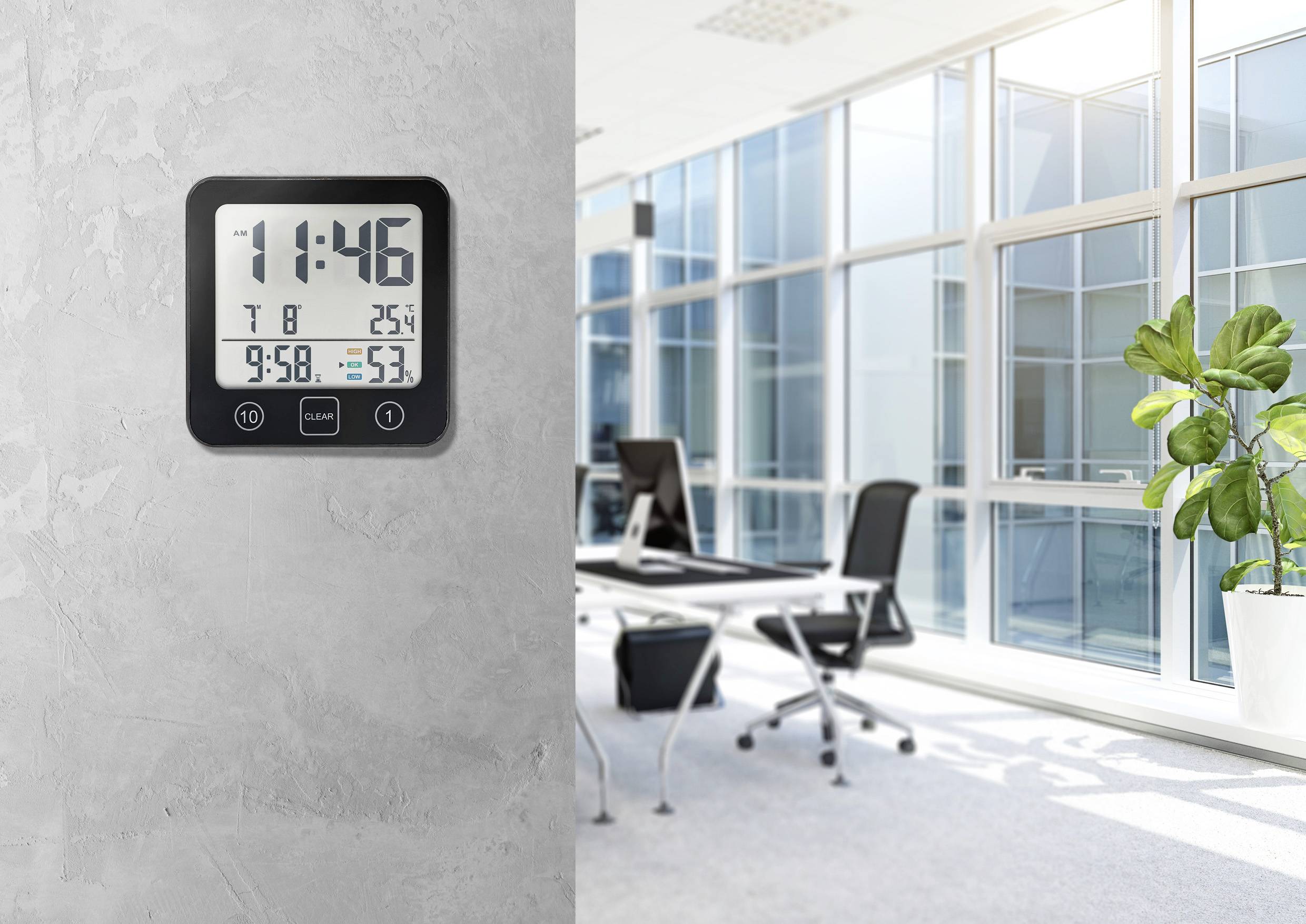 Digitální hodiny na betonové stěně v moderní kanceláři ukazují 11:46. Teplota: 25°C, vlhkost: 53%. V pozadí kancelář s pracovními stoly a rostlinami.