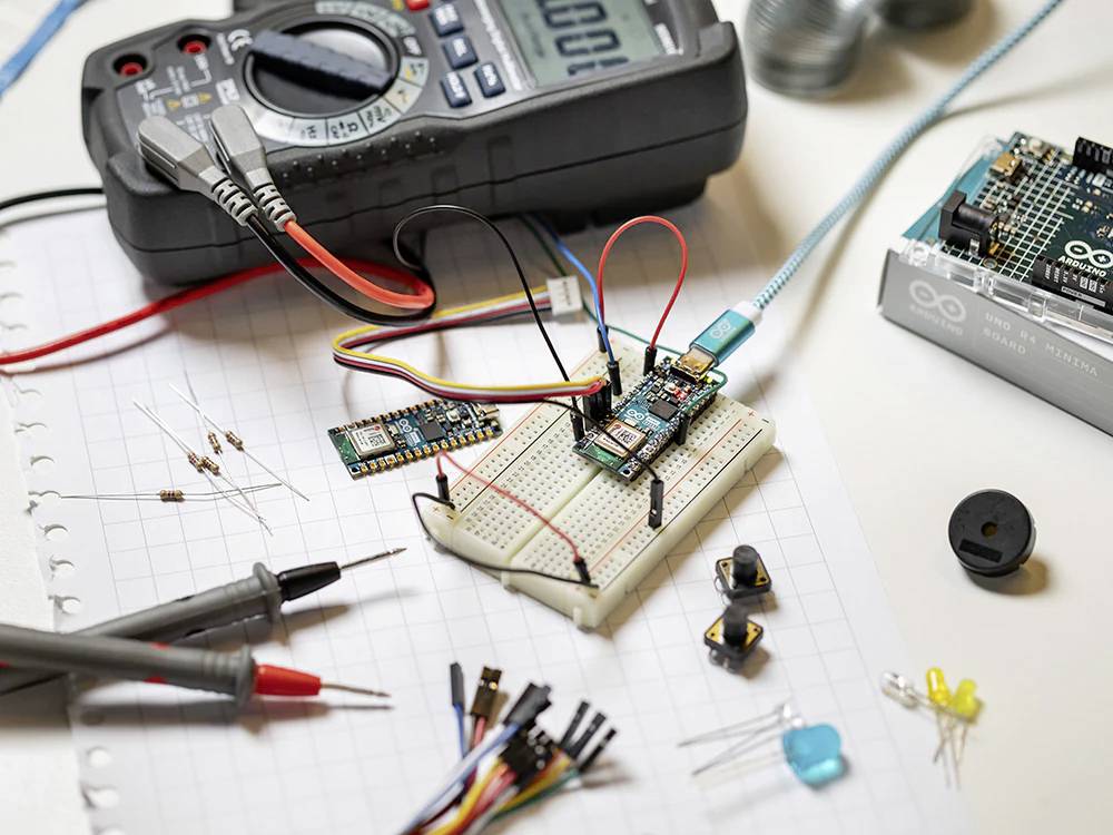 Elektronický obvodový projekt na stole, skládající se z nepájivého kontaktního pole, odporů, multimetru a komponent Arduino.