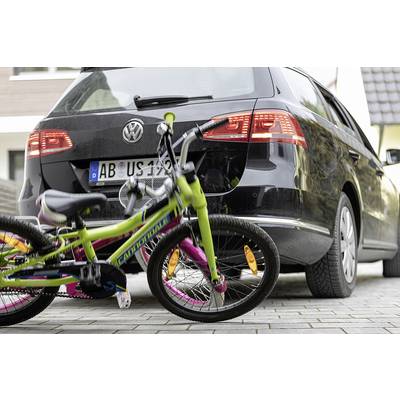 Jízdní kolo leží na chodníku za zaparkovaným autem. Kolo je barevné a auto je černé.