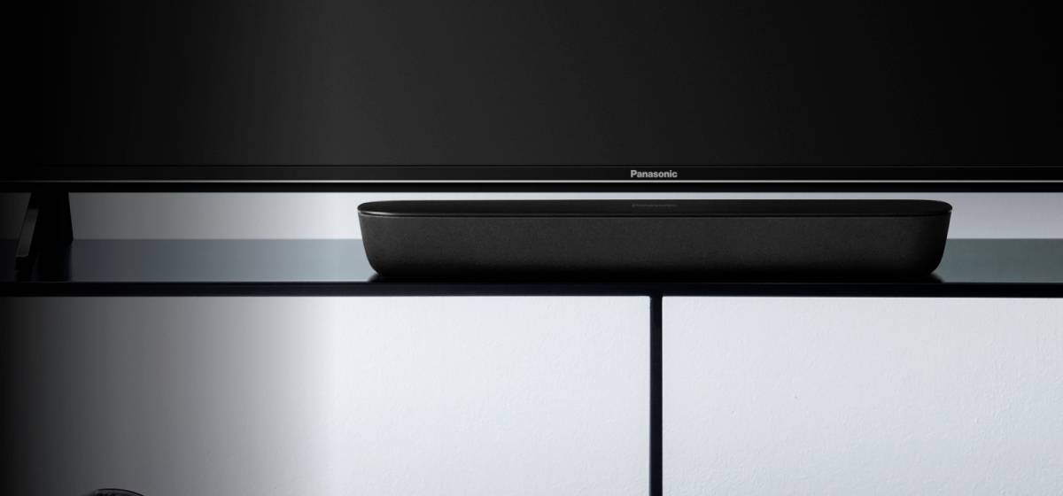 Plochý televizor stojí na moderní černé komodě. Pod ním je umístěna úzká černá soundbar.