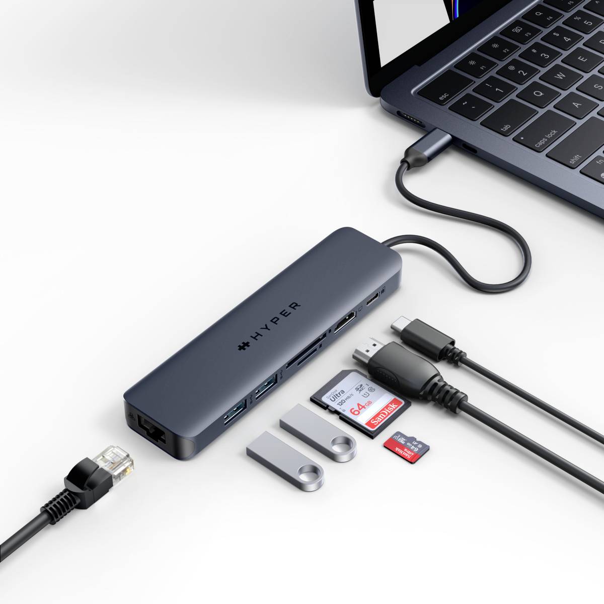 Laptop je připojen k USB rozbočovači, který má několik portů, včetně USB, HDMI, Ethernetu a slotů pro SD karty.
