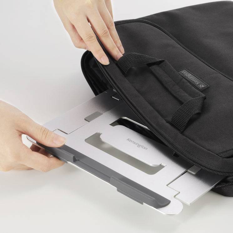 Jedna osoba vkládá stříbrný stojan na notebook do černé tašky.
