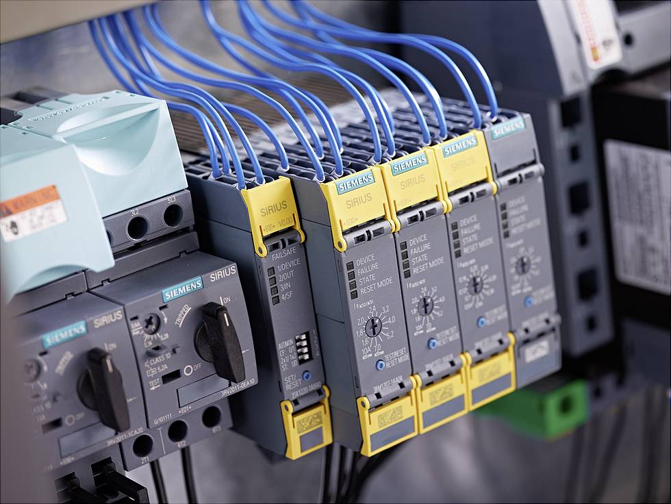 Několik spínacích přístrojů Siemens SIRIUS se žlutými a modrými kabely. Spínací přístroje jsou nainstalovány v technickém zařízení.