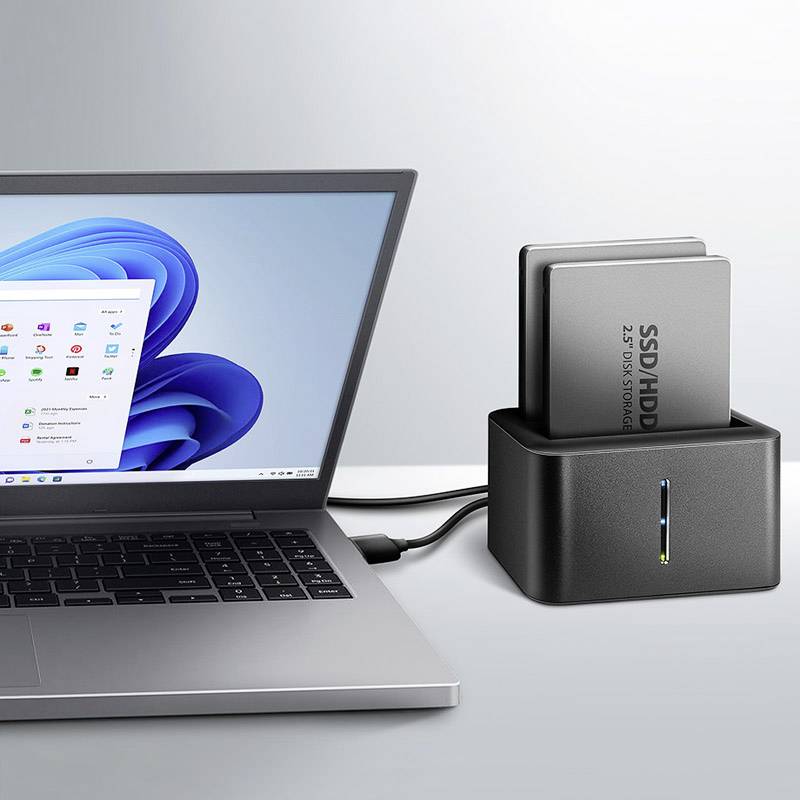 Notebook s otevřeným víkem a viditelnou obrazovkou, vedle něj dokovací stanice pro HDD/SSD se dvěma zapojenými pevnými disky, propojená přes USB.