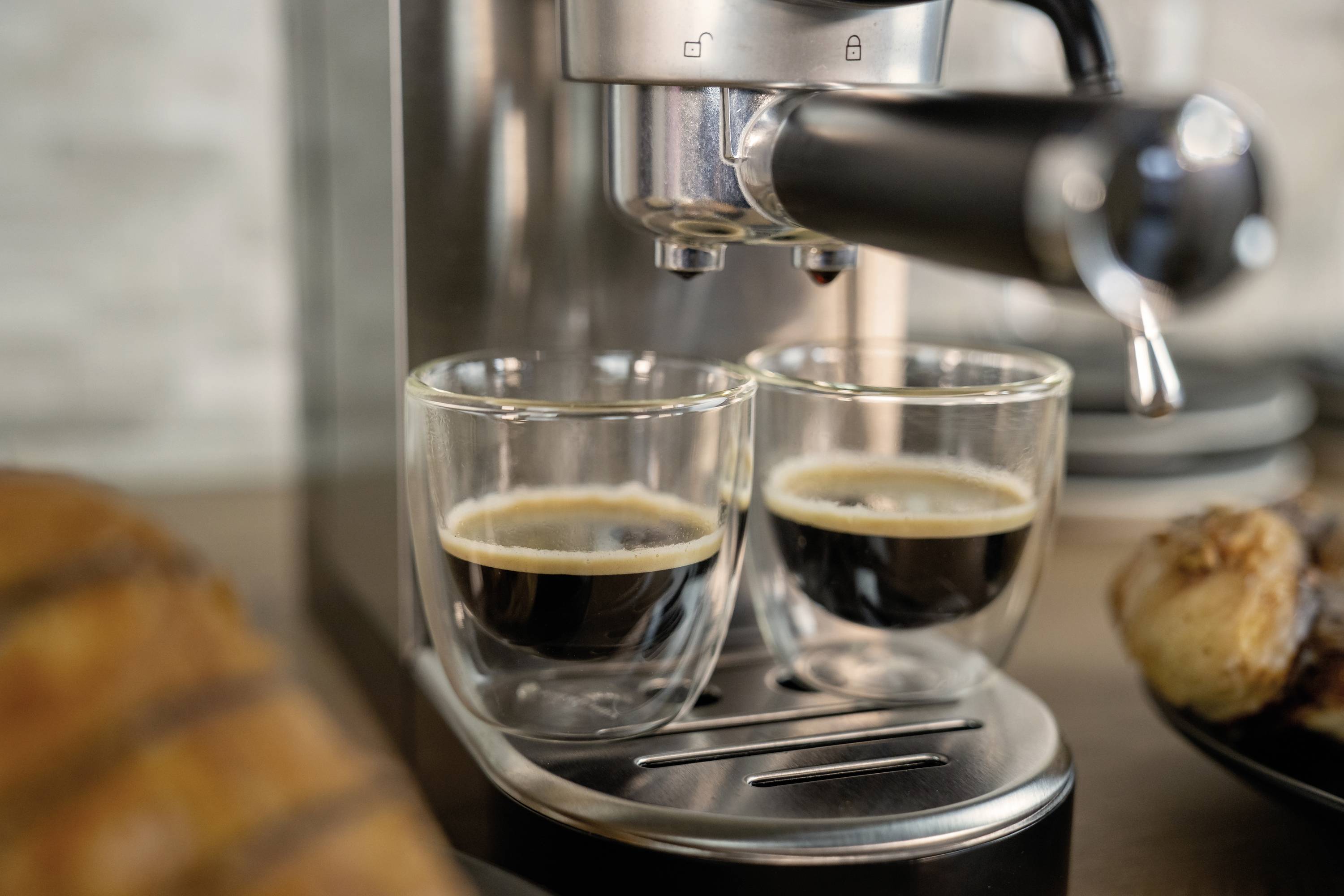 Espresso machine, která připravuje dva šálky espresa současně, v popředí jsou talíře s pečivem.