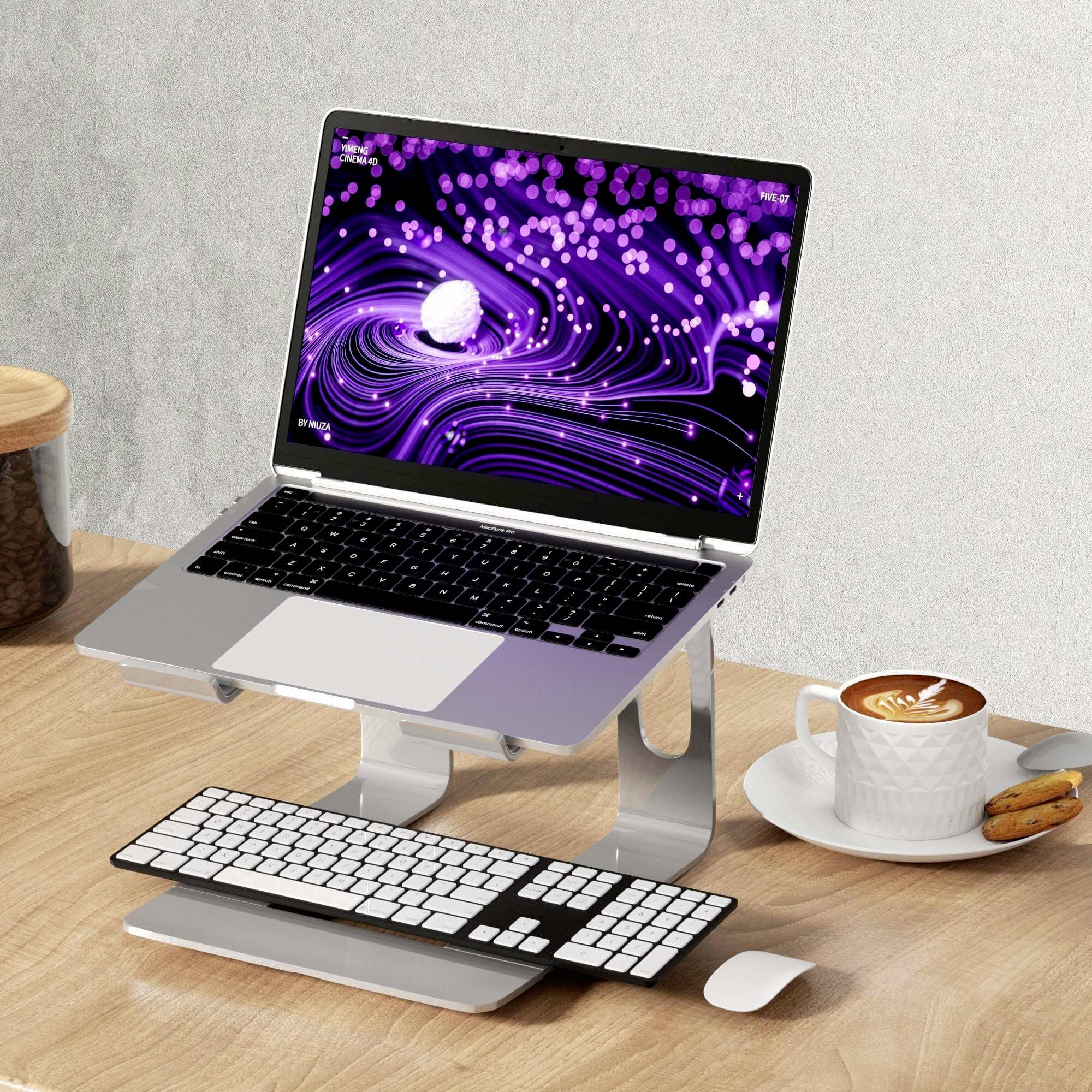 Laptop na psacím stole zobrazuje fialovo-bílý abstraktní vzor na obrazovce. Vedle něj stojí šálek kávy a sušenky.