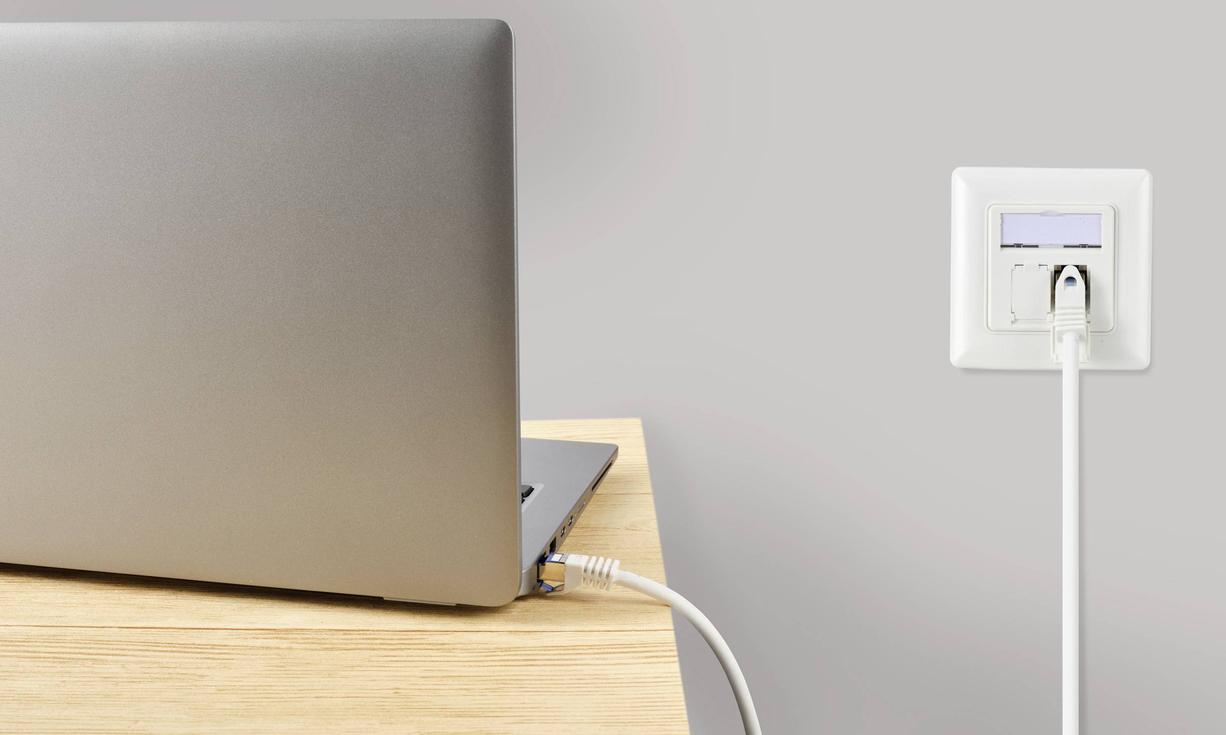 Laptop je připojený síťovým kabelem do nástěnné zásuvky vhodné pro internetové připojení.