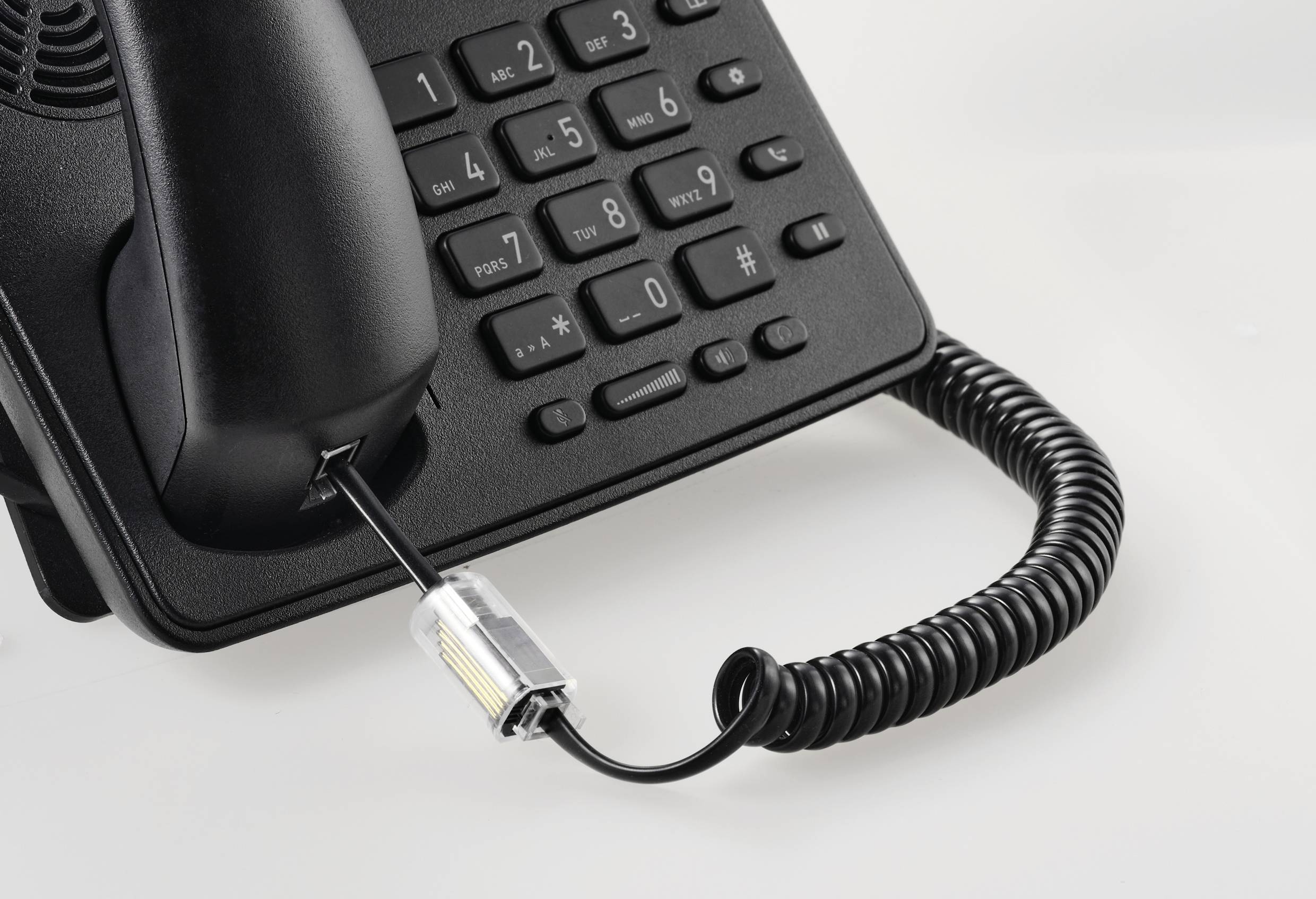 Černý kancelářský telefon se šňůrou, numerickou klávesnicí a sluchátkem položeným v základně. Kabel je spirálovitě stočený.