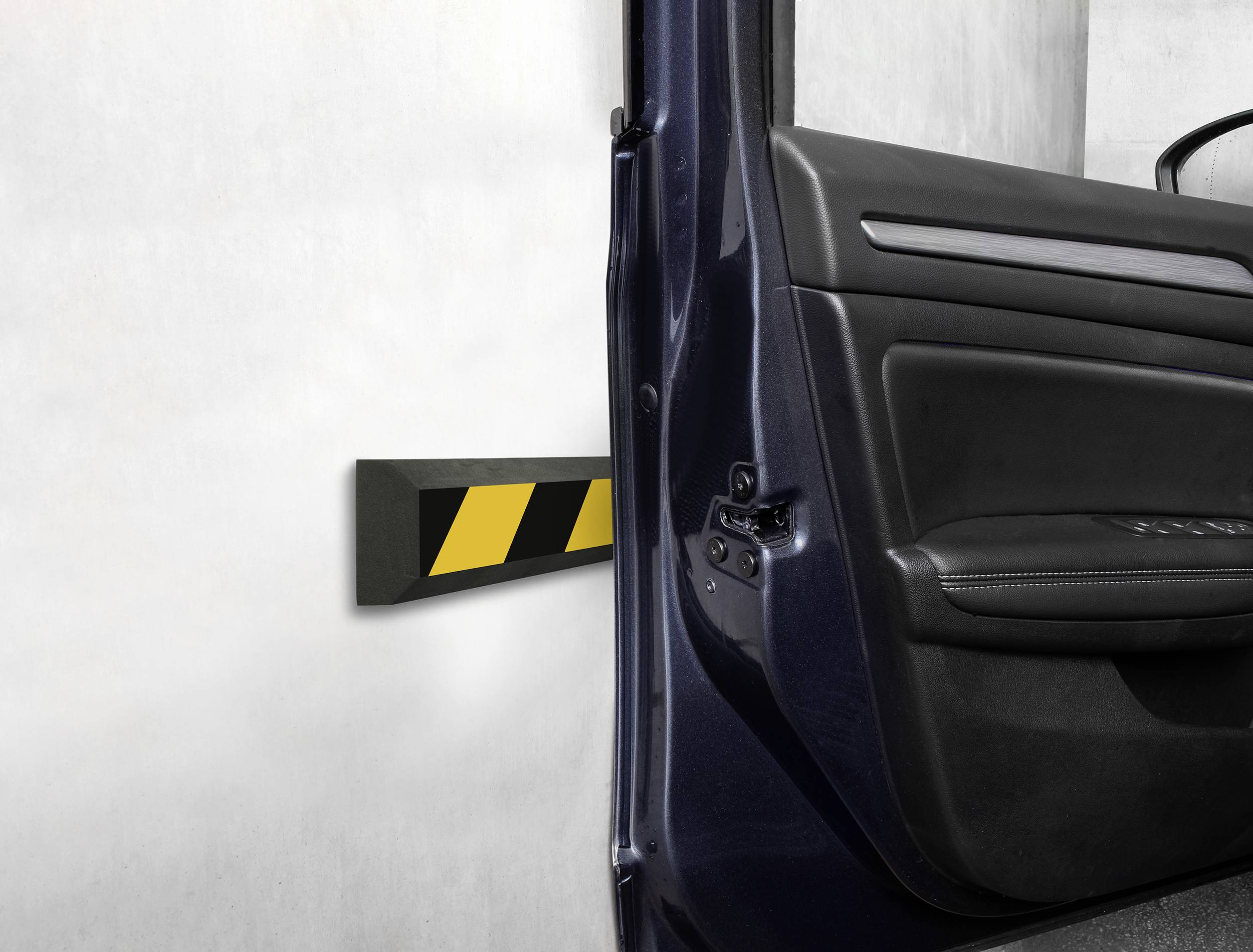 Otevřené autové dveře ukazují černý ochranný polštář s žlutými pruhy na betonové zdi, který slouží k prevenci promáčknutí.