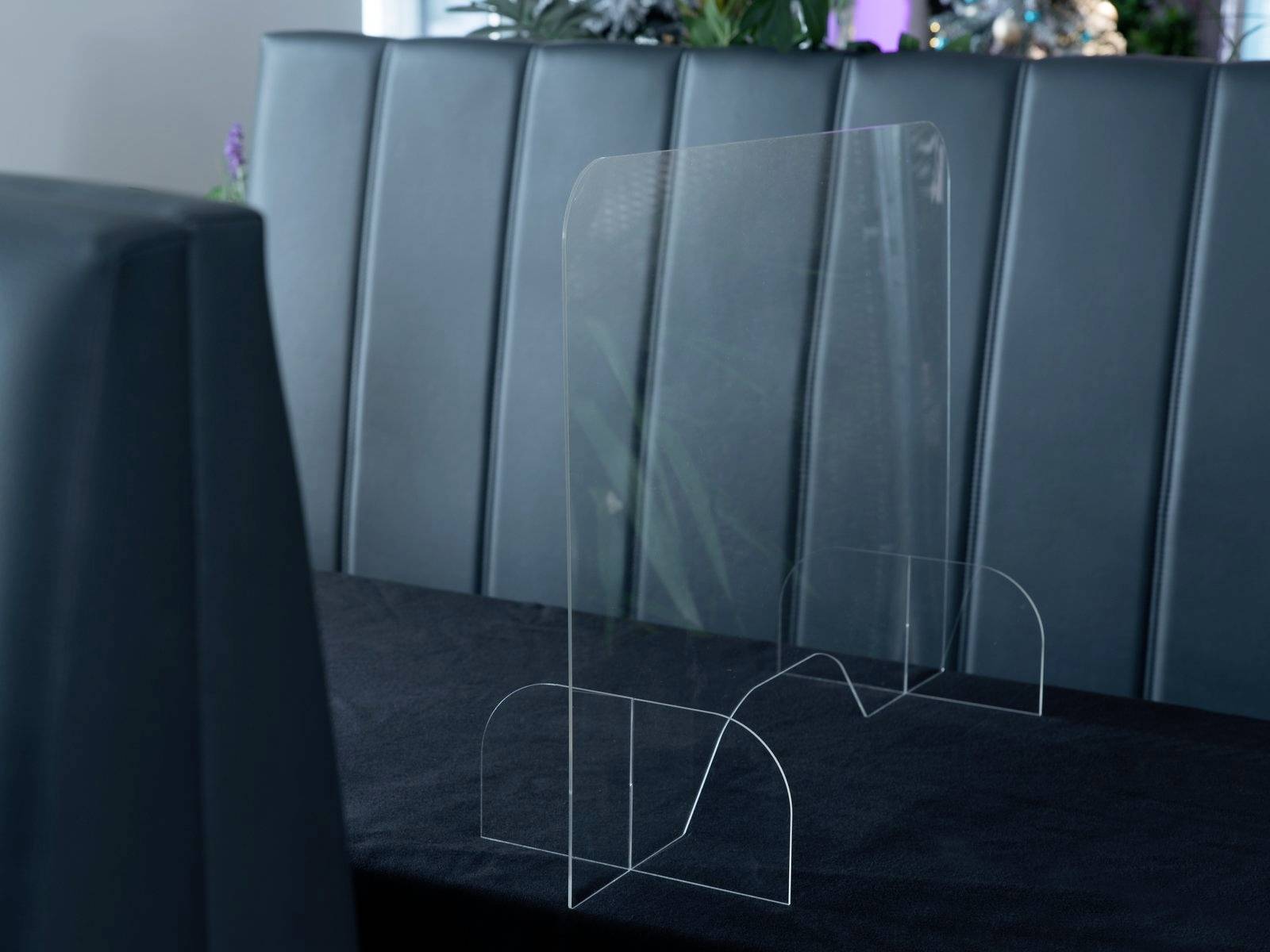 Průhledná dělicí zástěna na jídelním stole v restauraci odděluje místa k sezení.