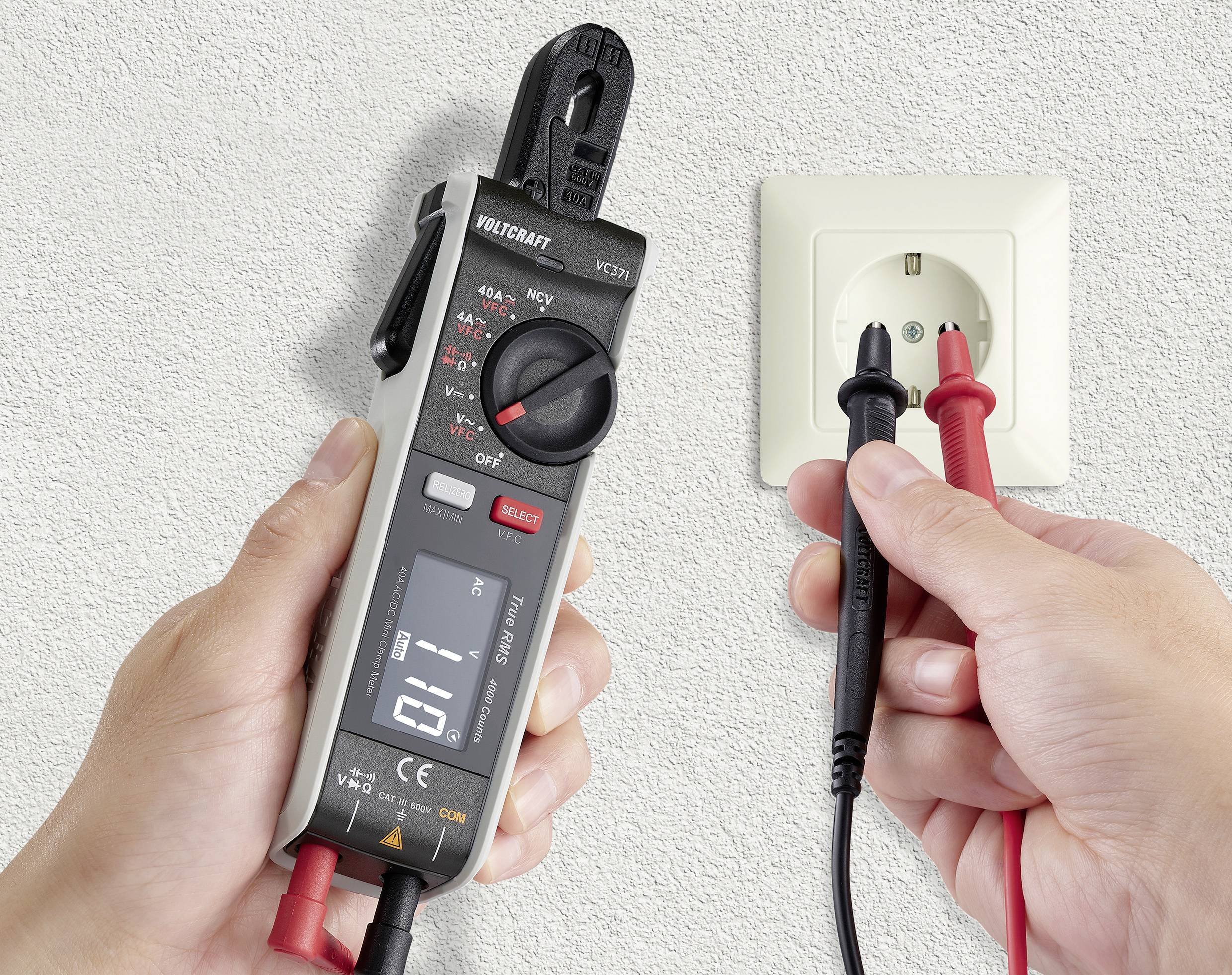 Jedna osoba měří napětí elektrické zásuvky digitálním multimetrem. Přístroj zobrazuje na displeji '0,1 V'.