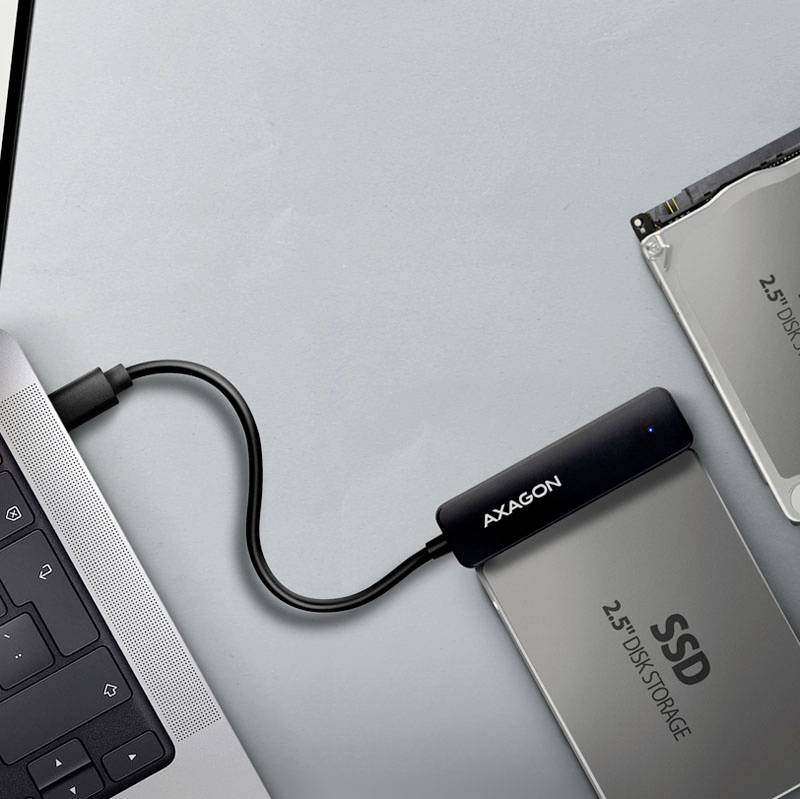 Externí SSD disk je připojena kabelem k notebooku. Displej notebooku a klávesnice jsou částečně viditelné.