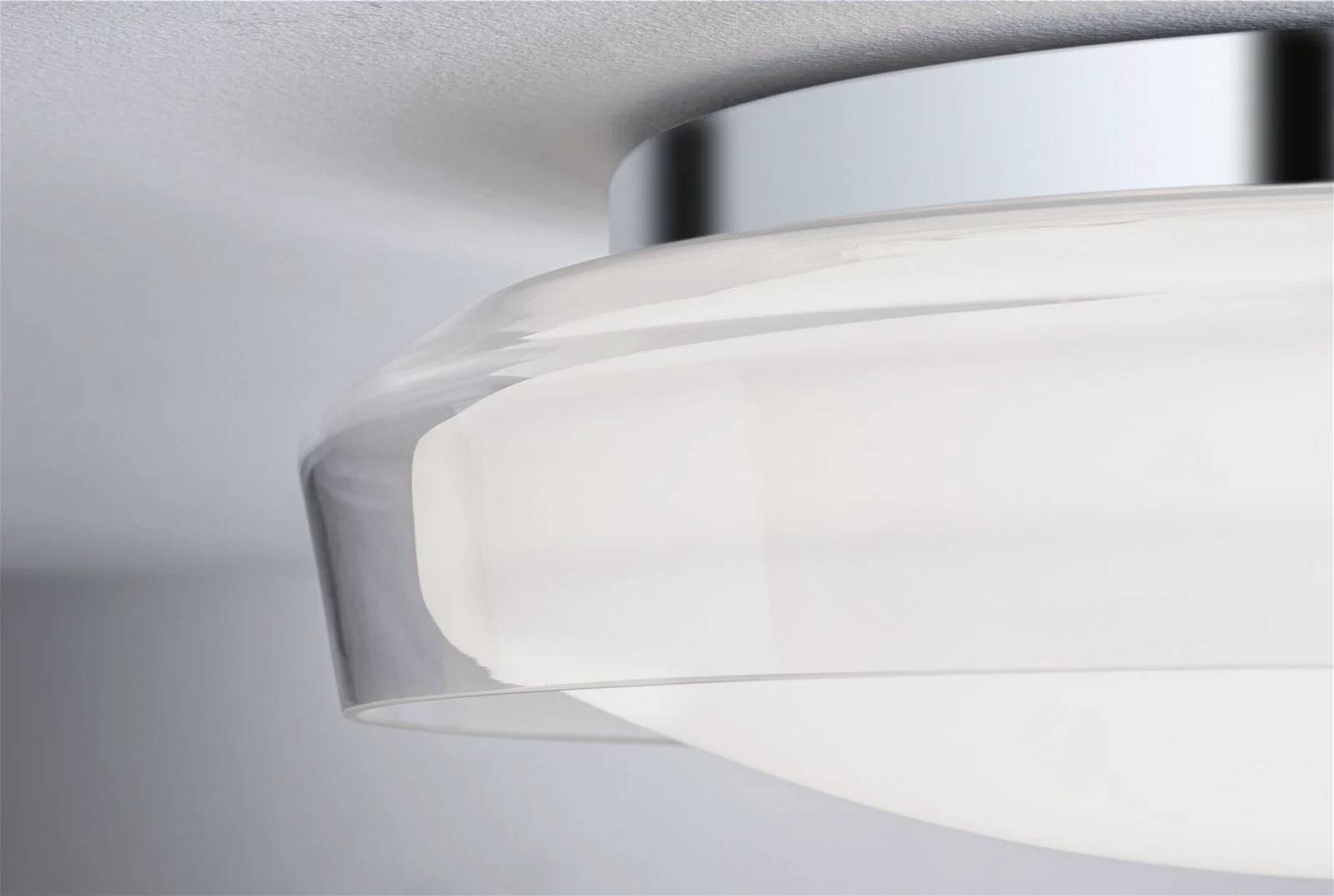 Detailní záběr moderního kulatého stropního svítidla s chromovým rámem a matně bílým sklem, namontovaného na šedém stropě.