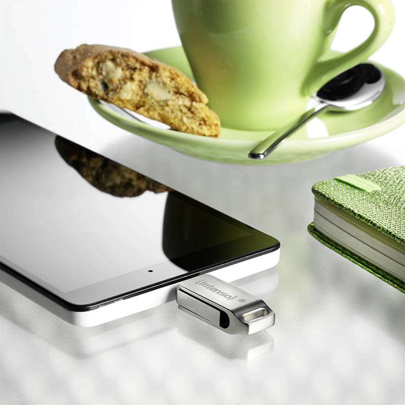 Smartphone s USB flash diskem, vedle zelený hrnek s sušenkou a zelený zápisník na stole.