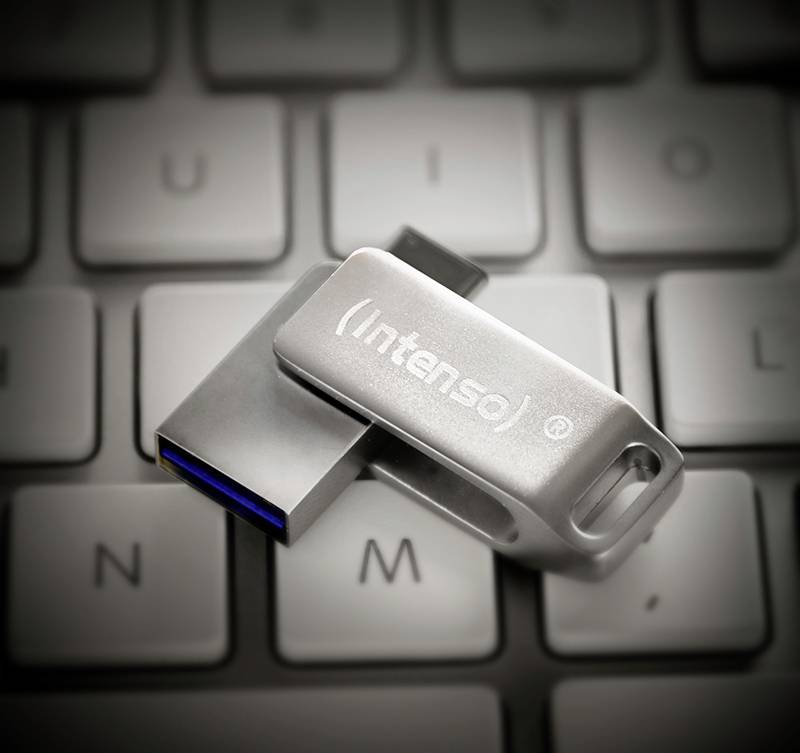 Na klávesnici notebooku leží stříbrný USB flash disk. Na disku je viditelné logo 'Intenso'.