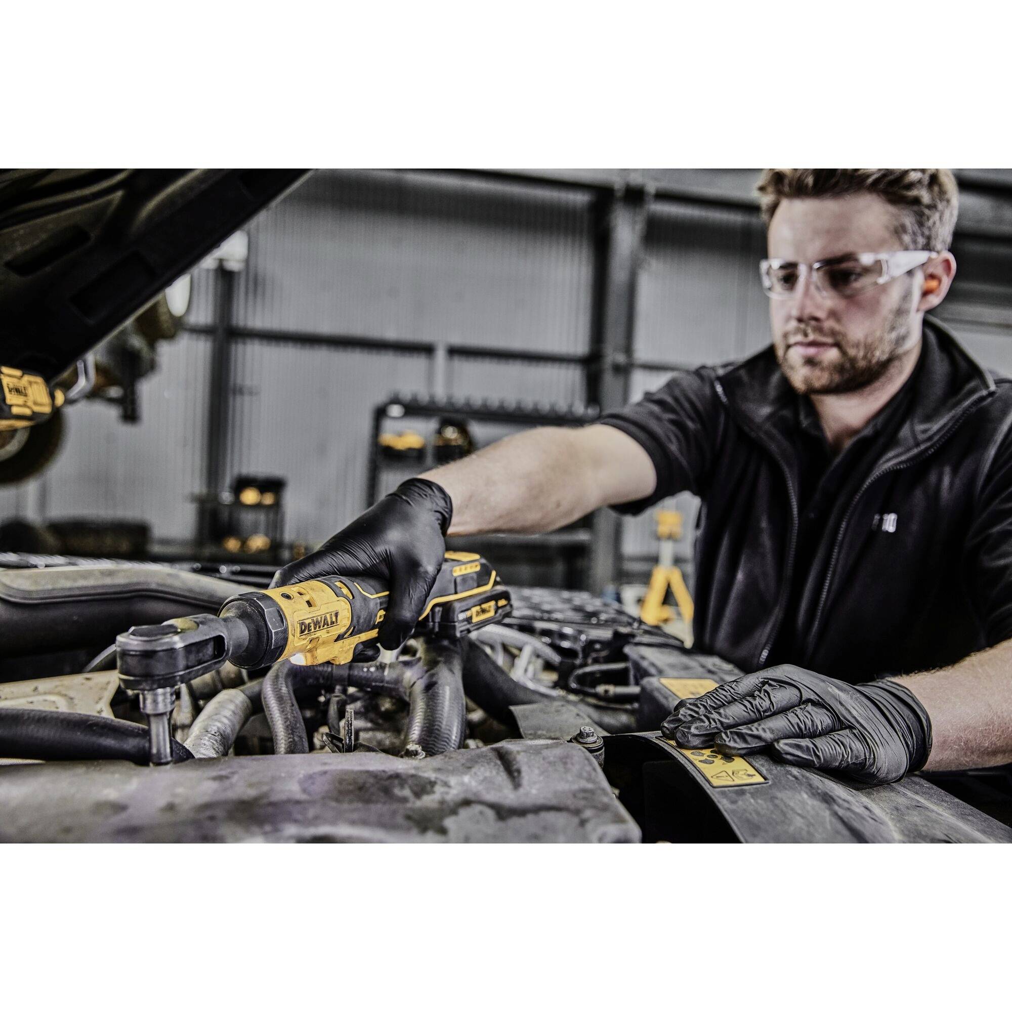 Mechanik v ochranných brýlích a rukavicích používá elektrický nástroj při práci na automobilovém dílu v motorovém prostoru.