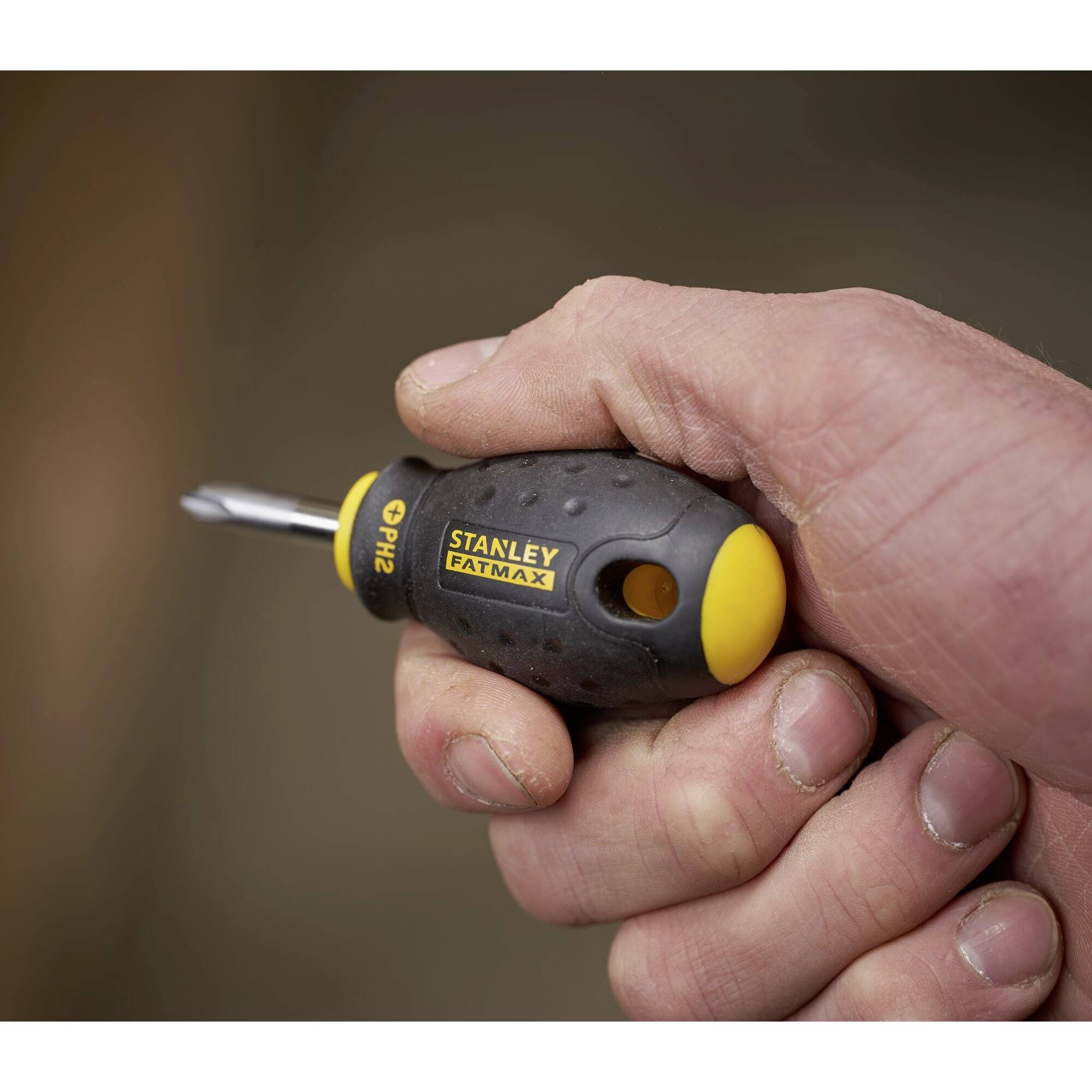 Jedna ruka drží černý šroubovák se žlutými detaily a nápisem 'Stanley Fatmax PH2', přičemž je zaostřeno na jeho rukojeť.