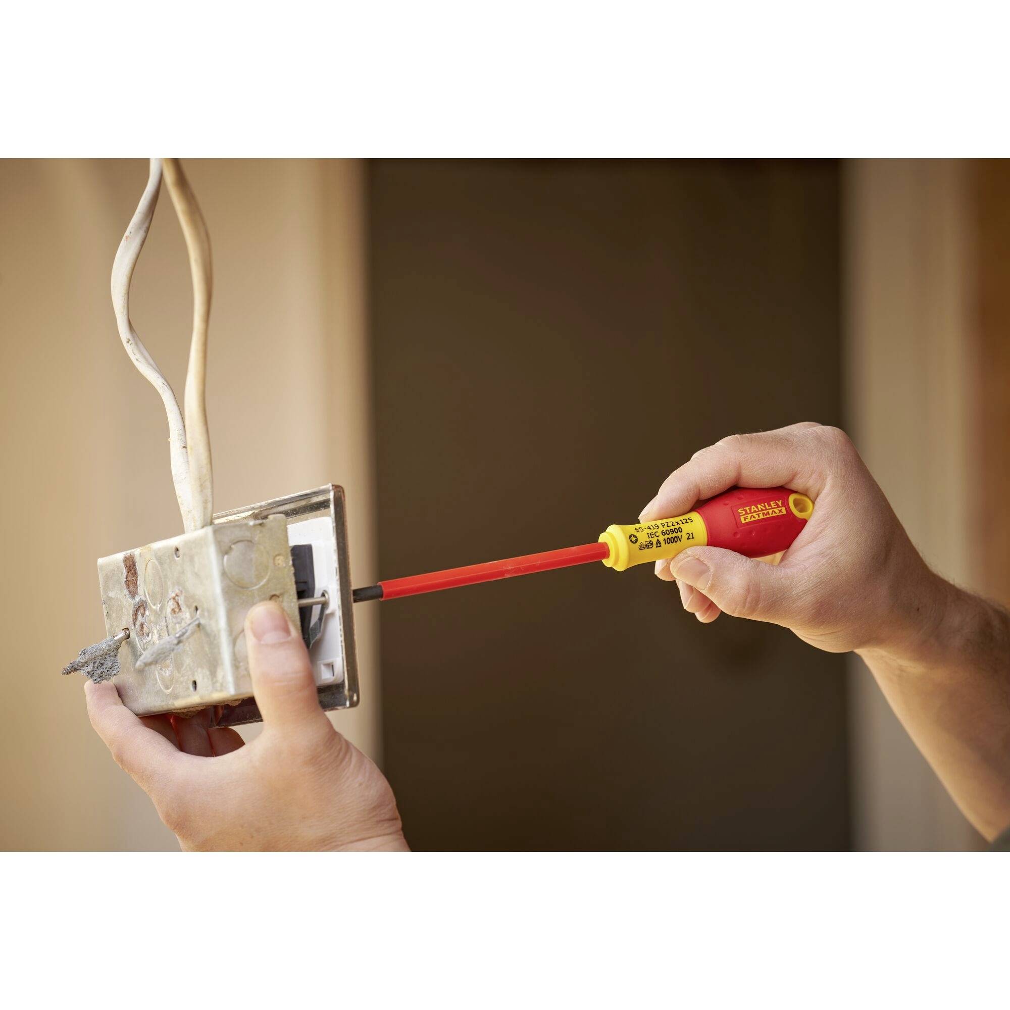 Osoba instaluje zásuvku a používá k tomu izolovaný šroubovák. V pozadí je viditelná stěna.