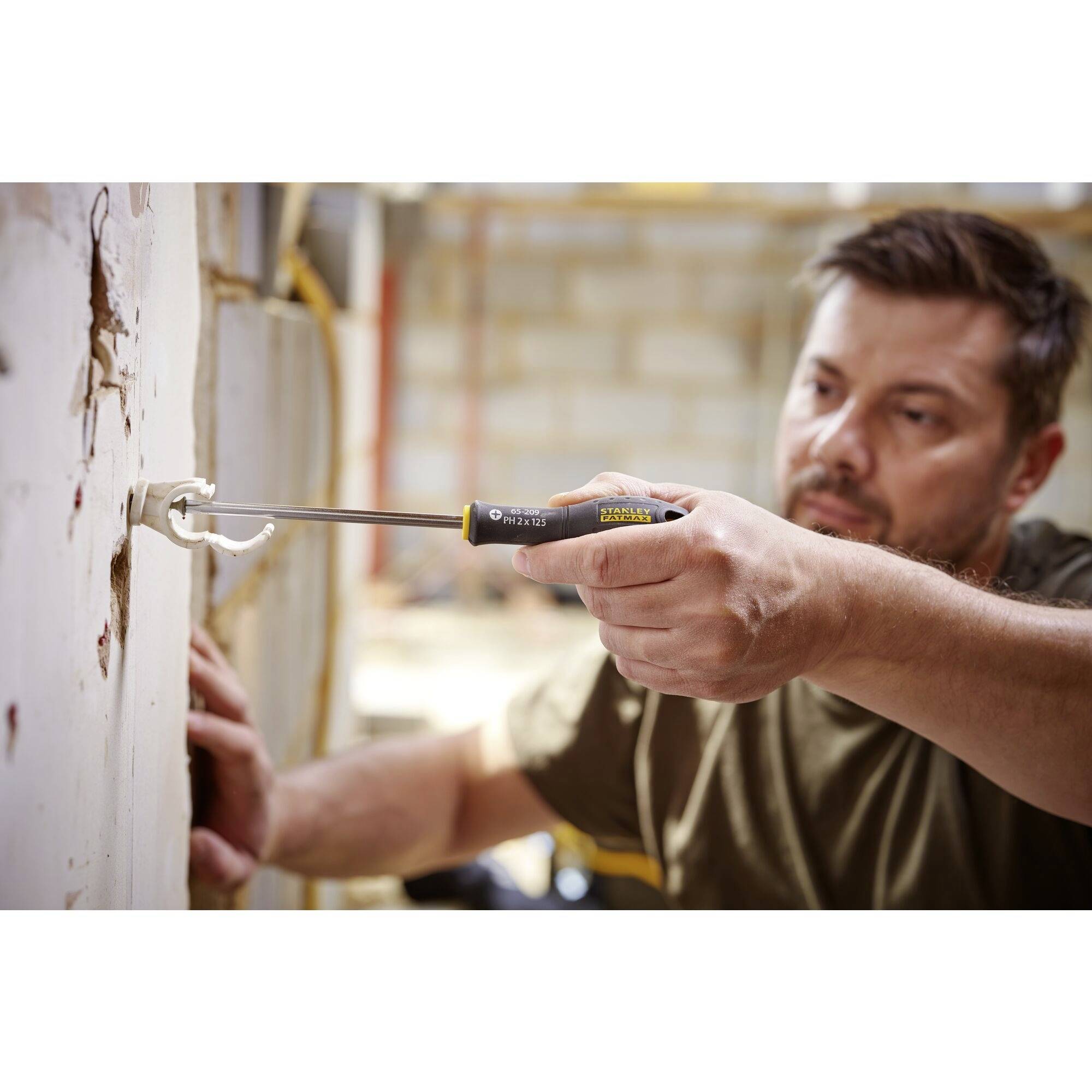 Muž používá šroubovák k vyjmutí šroubu ze zdi. V pozadí je viditelné staveniště.