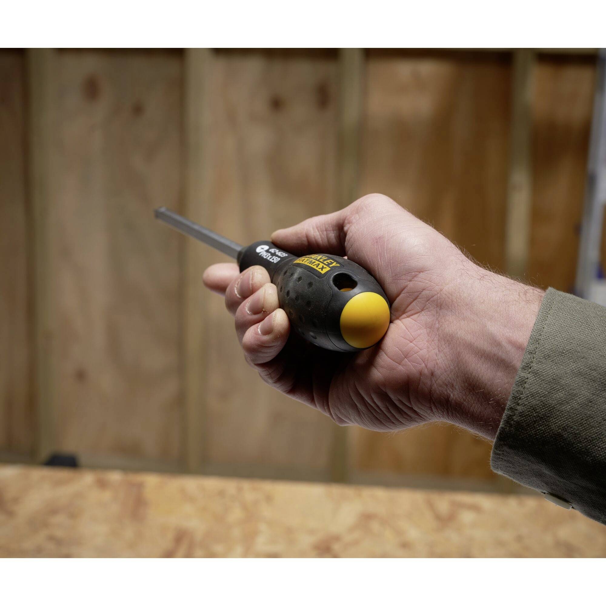 Jedna ruka drží šroubovák v dílně. V pozadí jsou vidět dřevěné stěny.