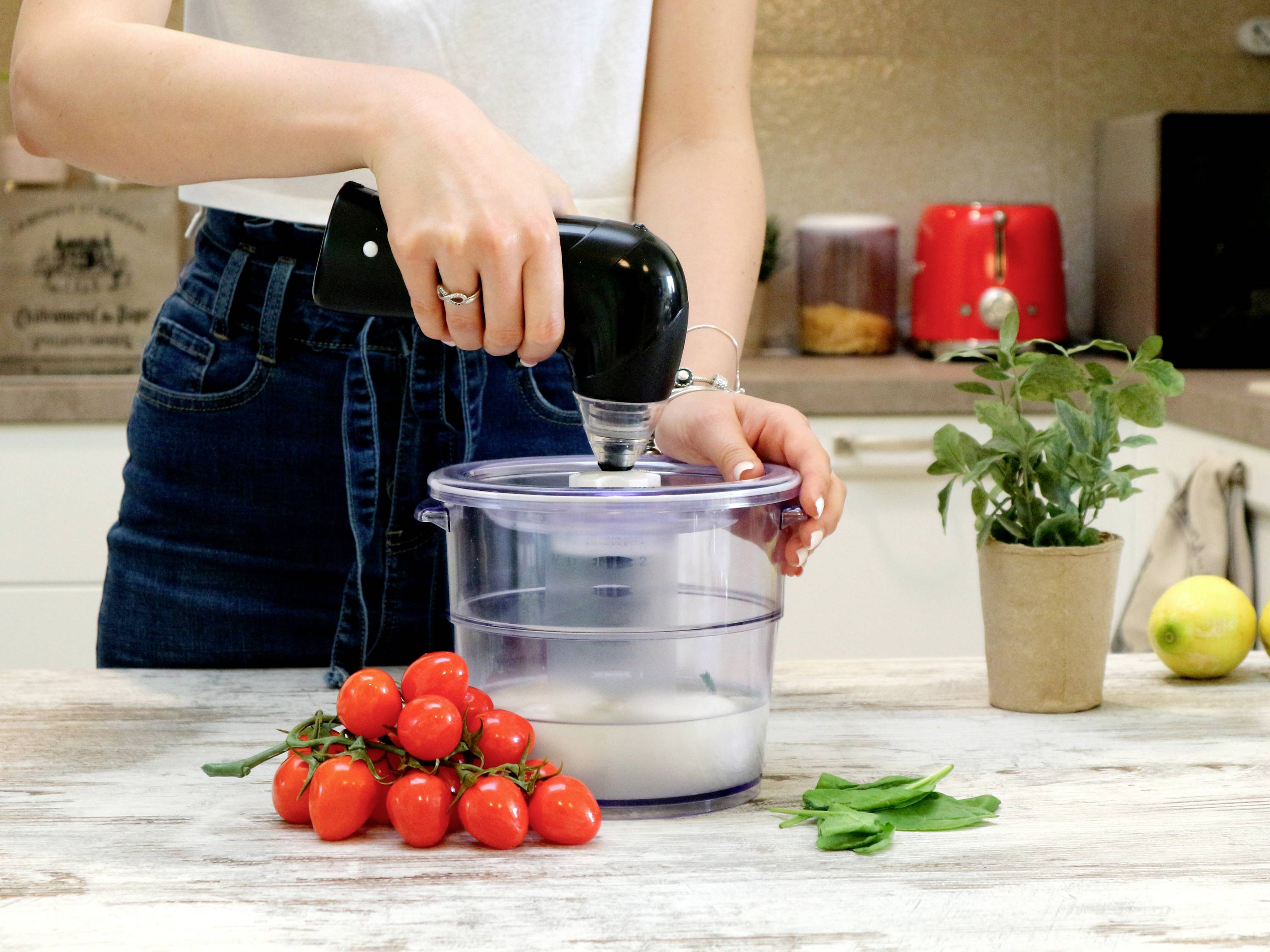 Osoba míchá něco ručním mixérem v průhledné míse. Vedle leží rajčata, bylinky a citron.