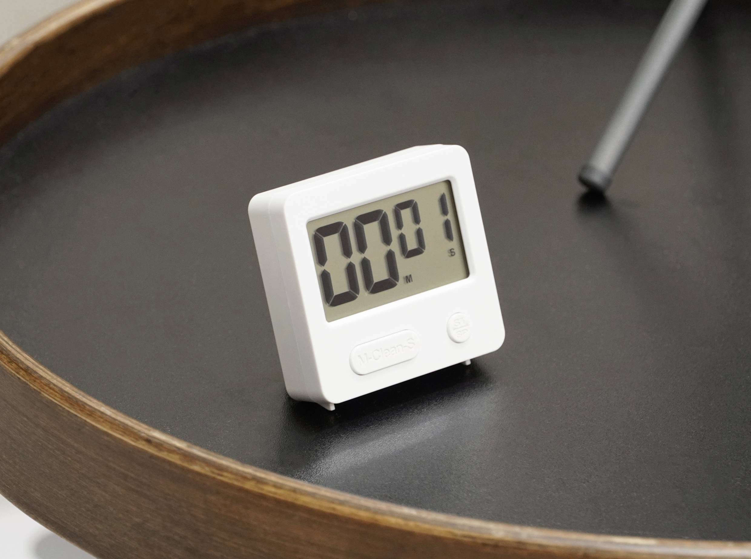 Digitální stopky na kulatém podnosu ukazují '00:01' sekund, vedle leží pero.