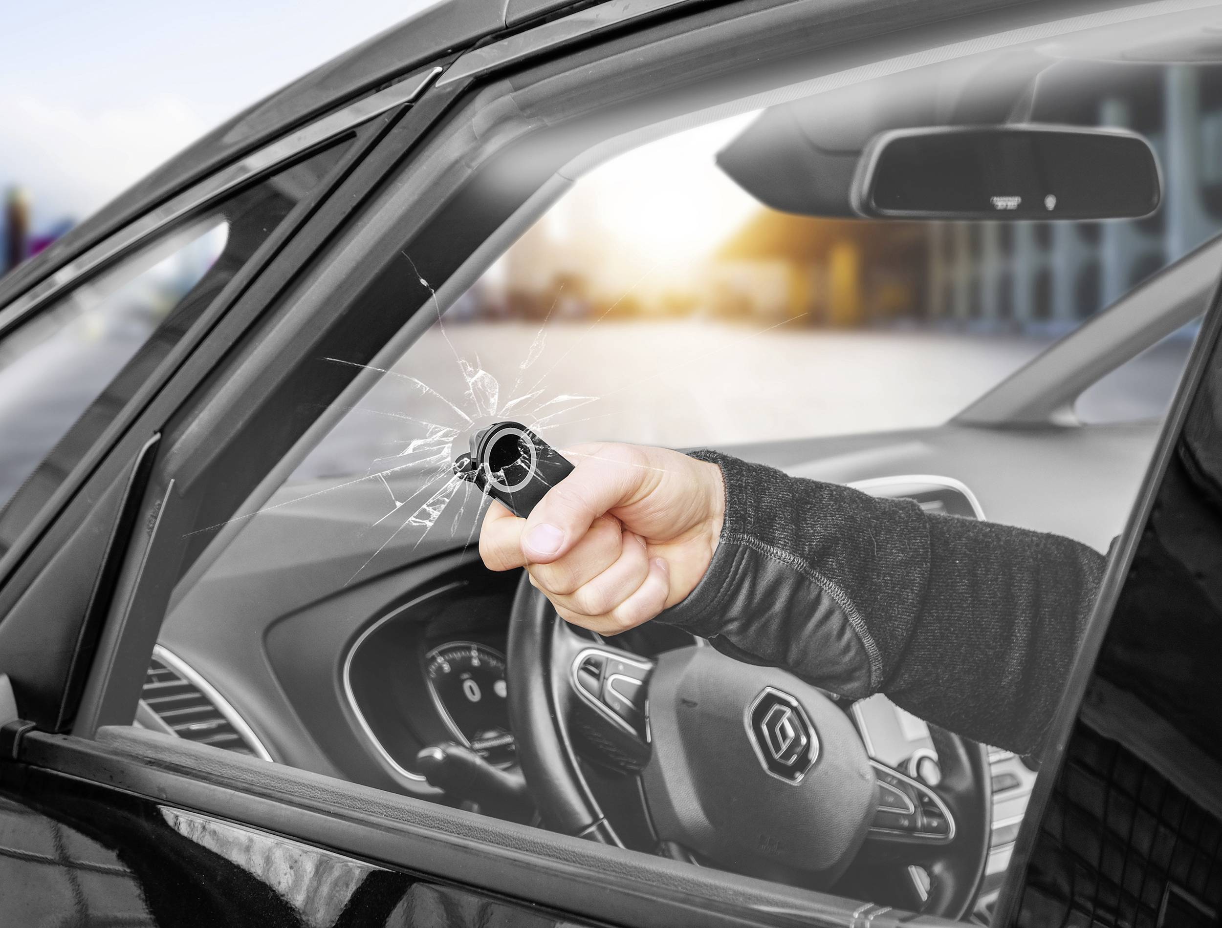 Osoba rozbíjí autové okno nástrojem. Vnitřek vozu je viditelný.
