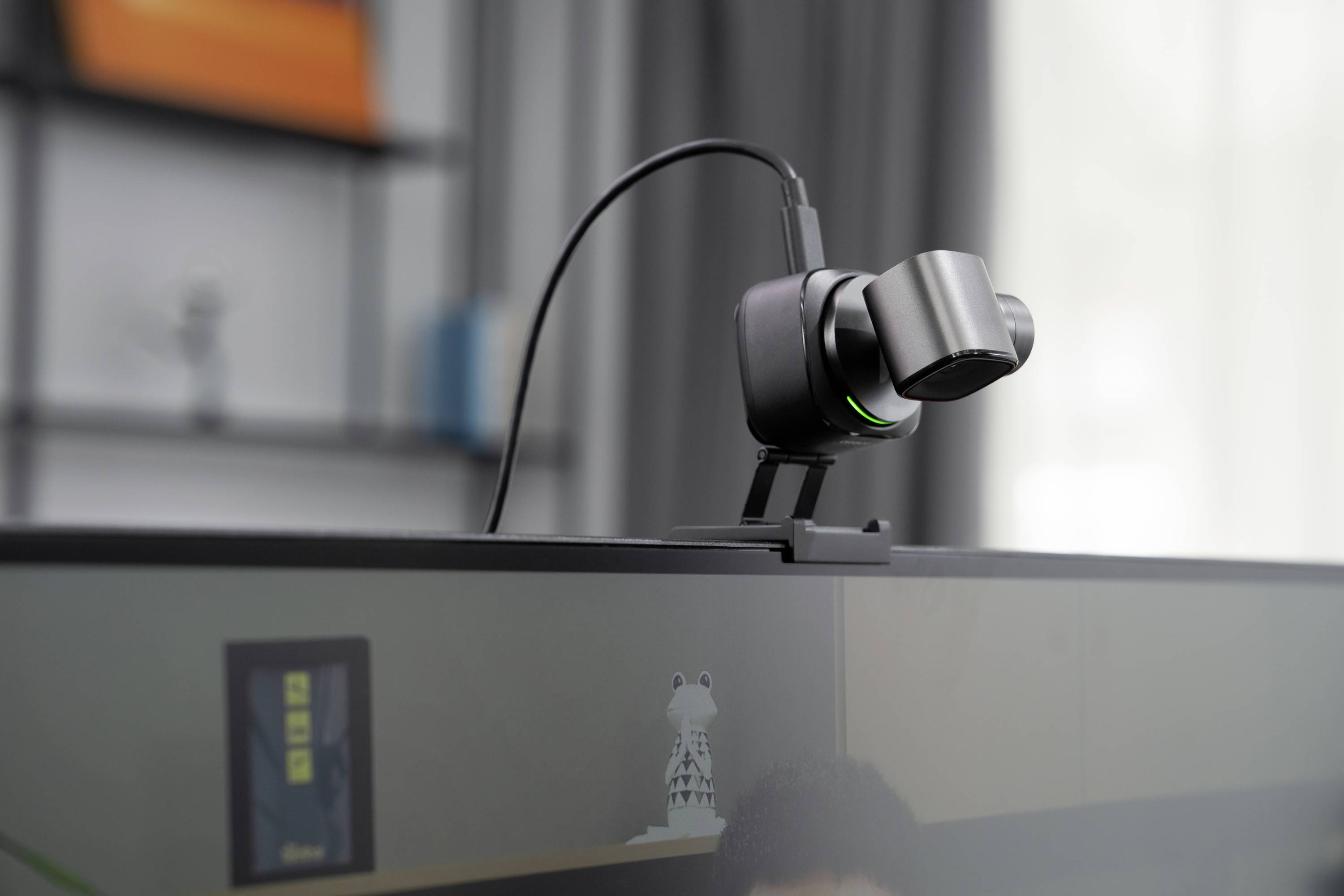 Webkamera je namontována nahoře na monitoru. Ukazuje černou skříňku s zeleným světlem a je připojena k kabelu.