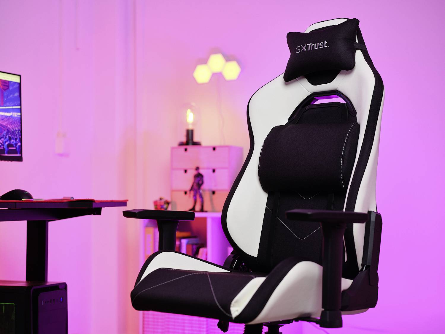 Herní židle v černobílém provedení, ergonomická s nastavitelnými opěrkami rukou, bederní opěrkou a hlavovou opěrkou v moderním osvětleném prostoru.