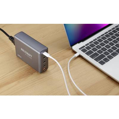Notebook je nabíjeno přes USB kabel z víceportové nabíječky na dřevěném stole.