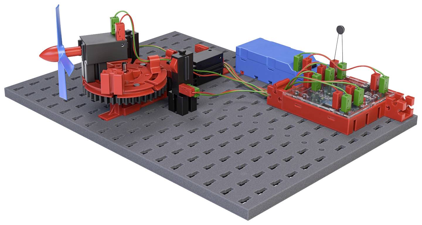 Model větrné turbíny s připojenými elektronickými komponenty na šedé platformě, který znázorňuje přeměnu obnovitelné energie.