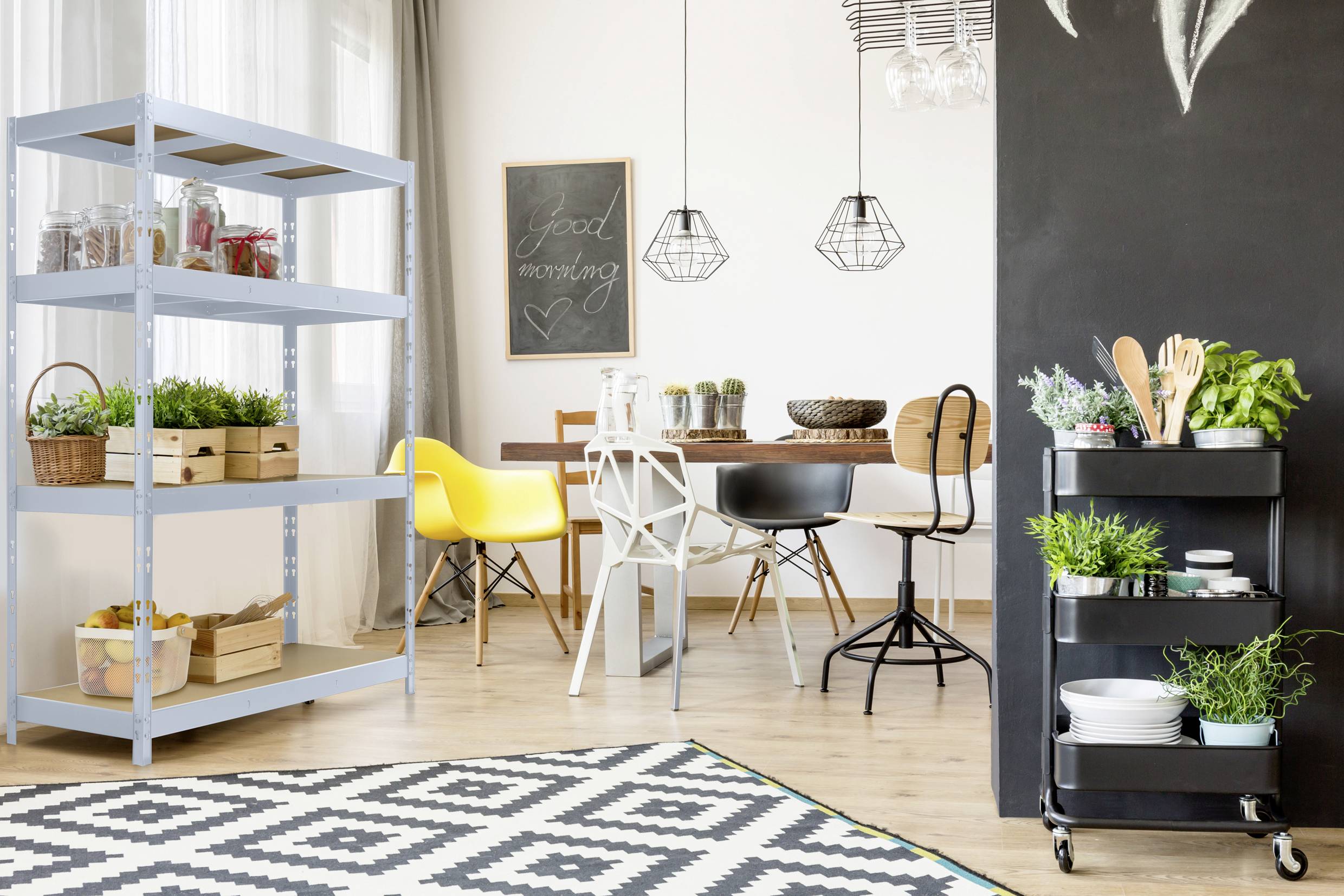 Jídelna se dřevěným stolem, černými a žlutými židlemi, policí plnou rostlin a servírovacím vozíkem. Na tabuli nápis 'Good Morning'.