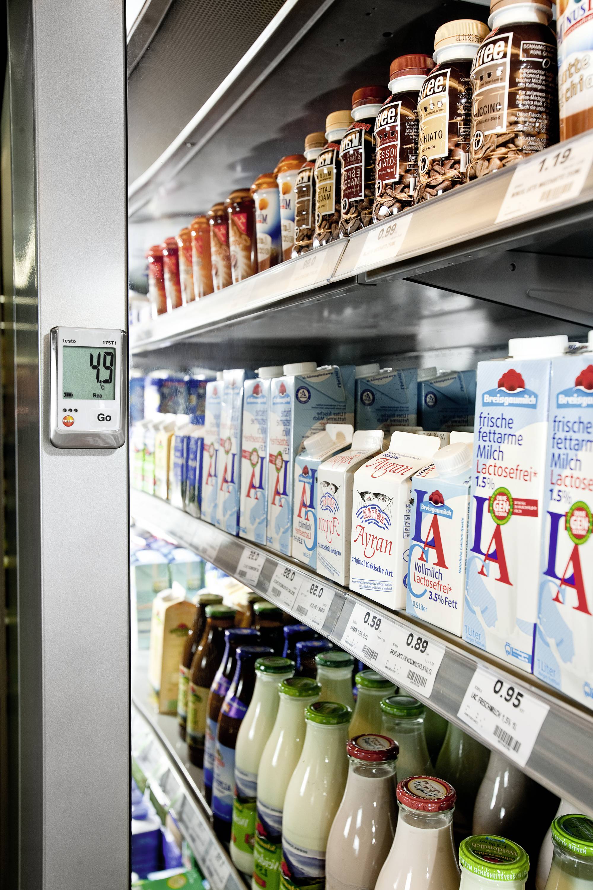 Chladící regál v supermarketu s různými nápoji, včetně mléka, jogurtů a čokoládového mléka. Teploměr ukazuje 4,9 stupňů Celsia.