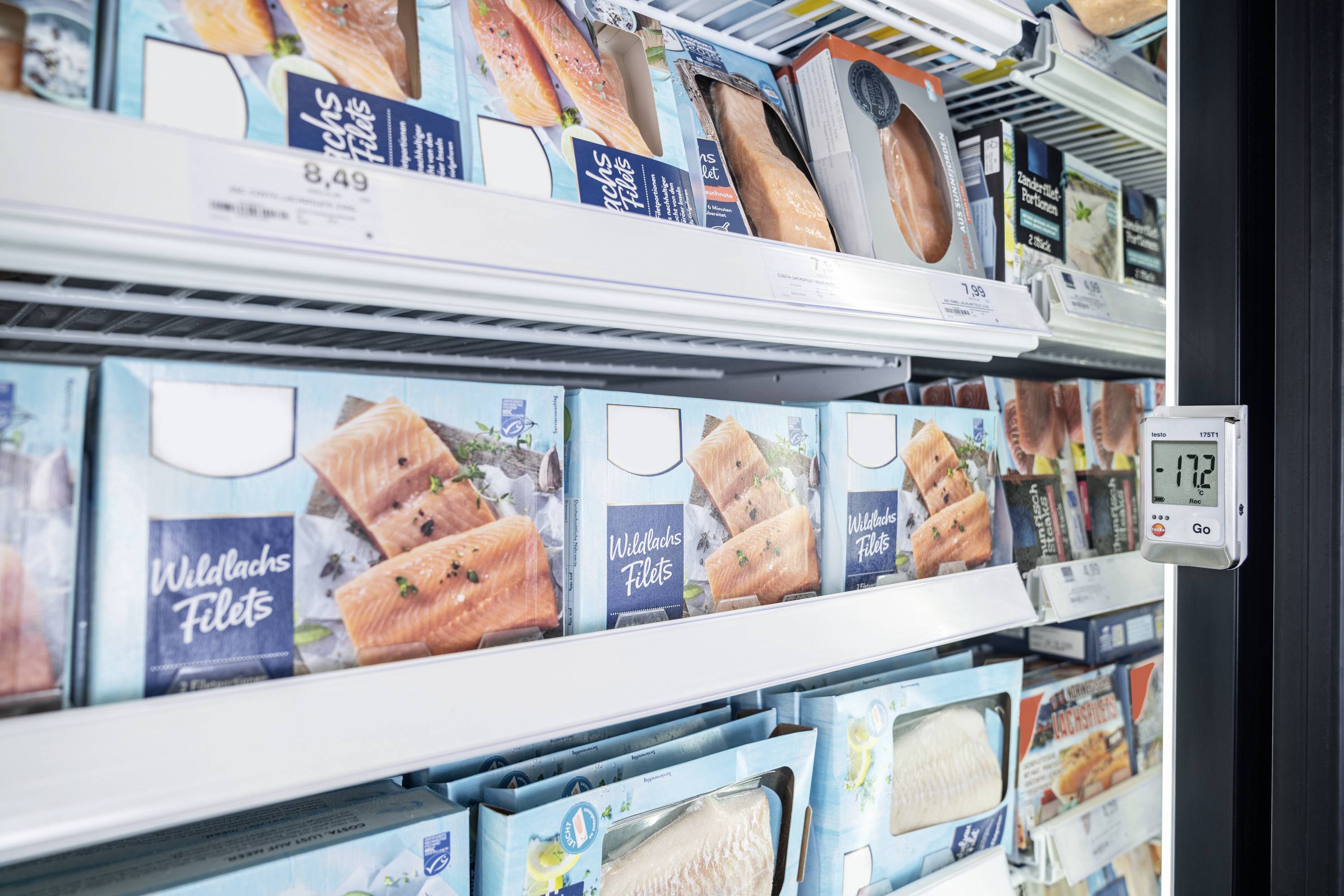 Mrazicí police v supermarketu s balíčky lososových filetů. Teploměr ukazuje teplotu -17,2 °C.