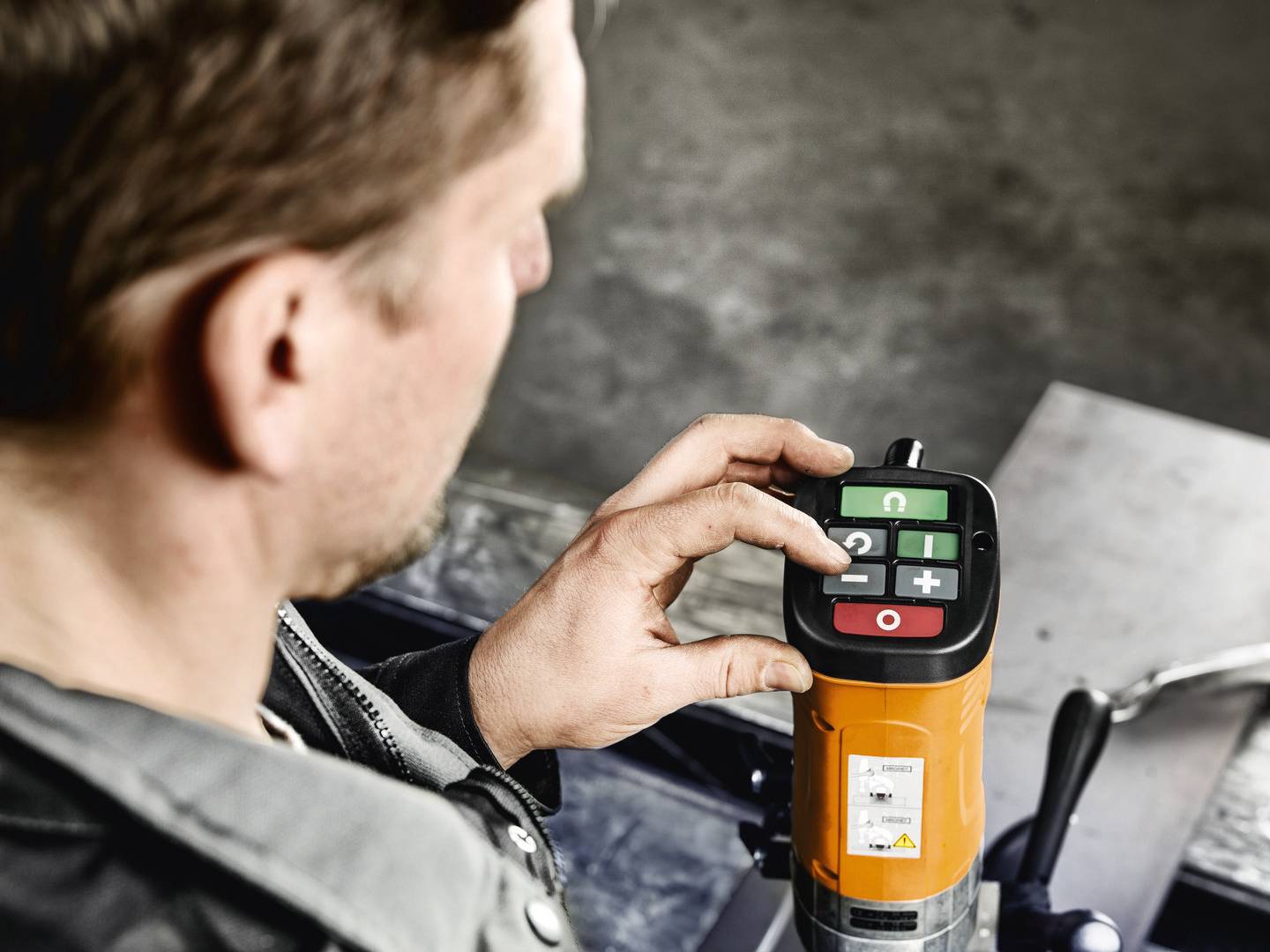 Muž obsluhuje elektronickou řídicí jednotku s displejem a tlačítky v barevném kódování, která je namontována na průmyslovém zařízení.