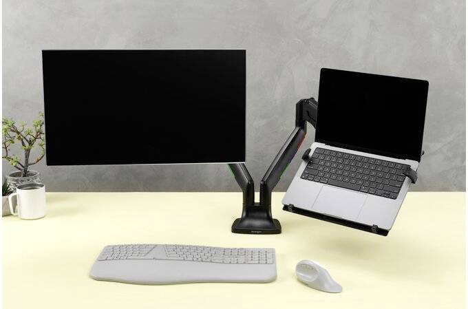 Psací stůl s monitorem a laptopem, oba upevněné na flexibilních ramenech. Vedle toho klávesnice, myš a rostlina.
