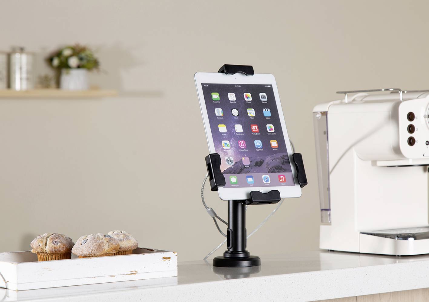 Tablet je umístěn ve stojánku na pracovní desce, vedle něj je kávovar a podnos s muffiny.