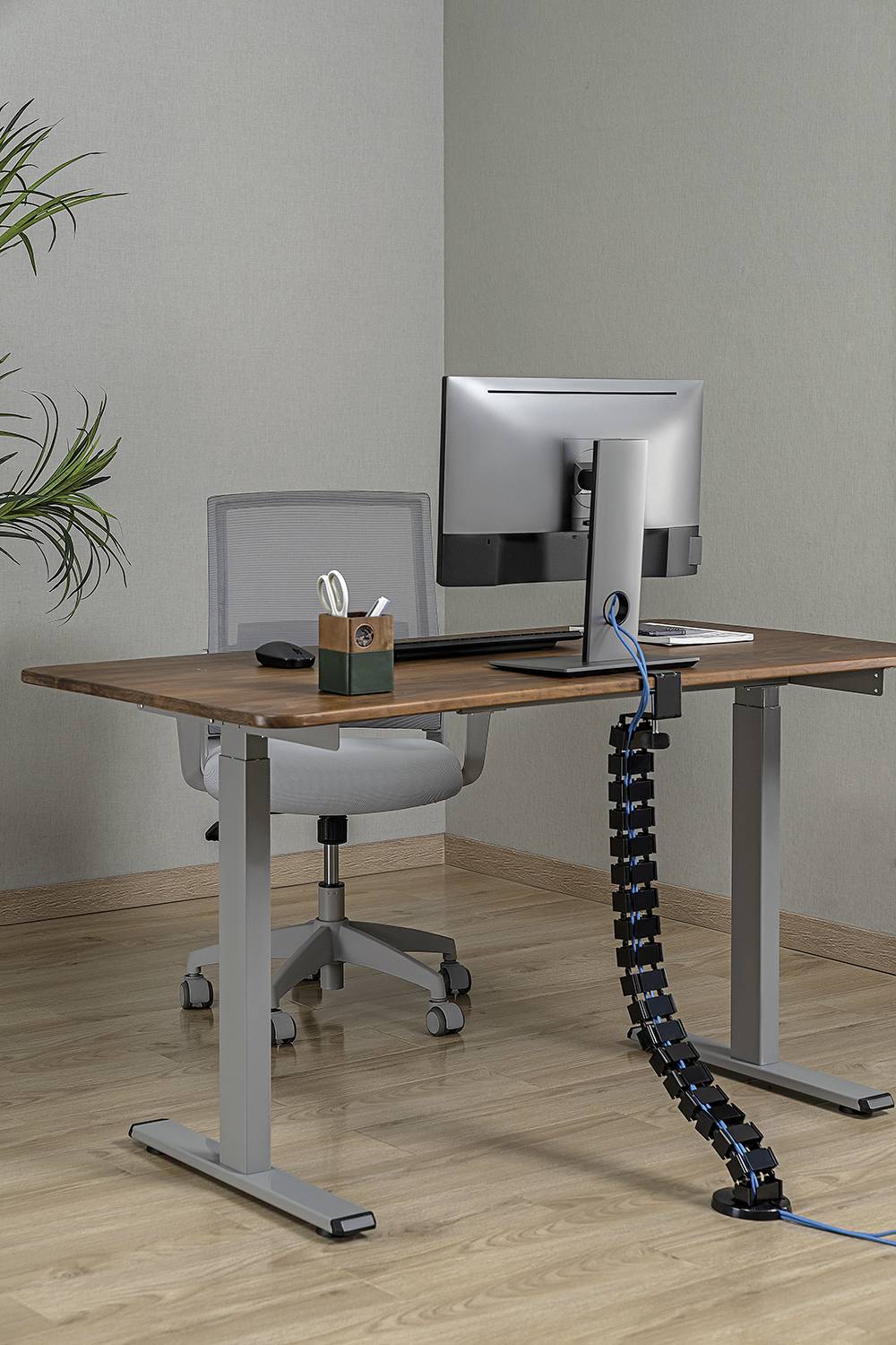 Moderní psací stůl s nastavitelnou výškou, vybavený počítačovým monitorem, klávesnicí a ergonomickou židlí.