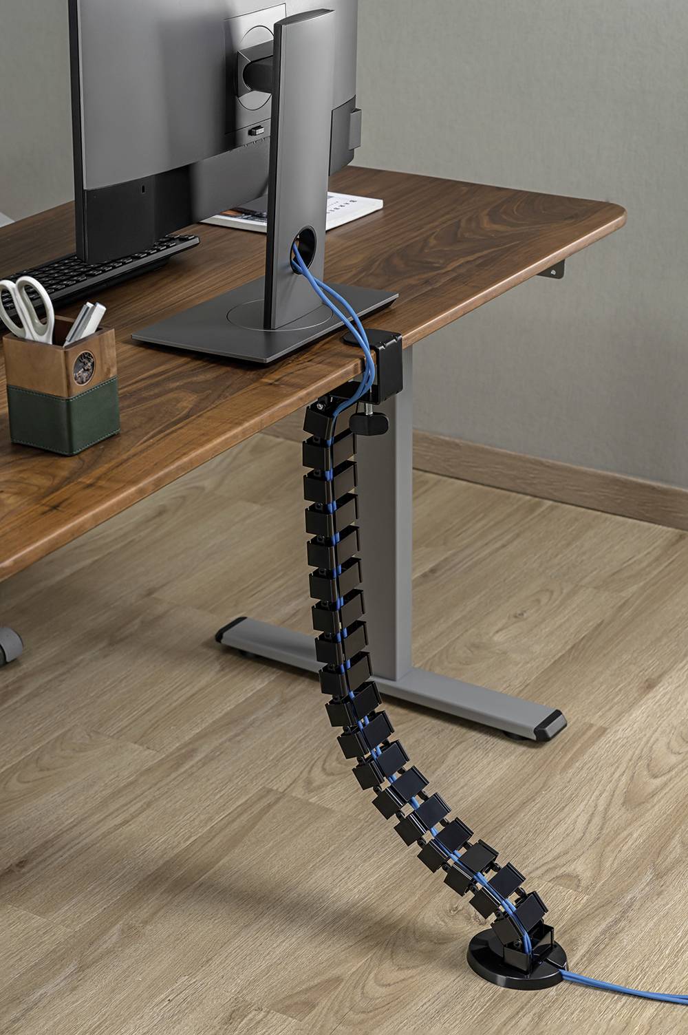 Správa kabelů na pracovním stole s monitorem. Kabely jsou uspořádaně vedeny flexibilním kabelovým kanálem dolů k podlaze.