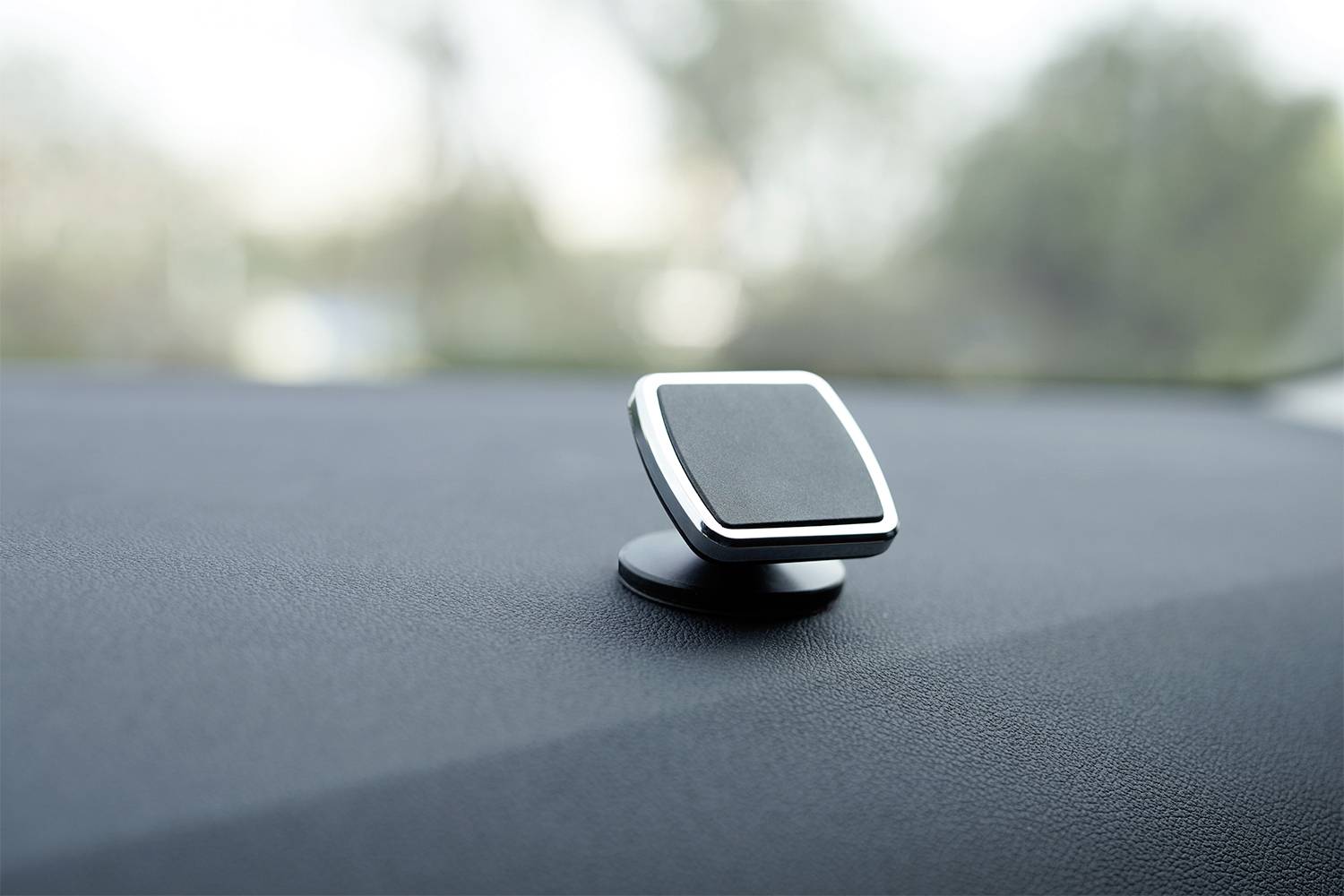 Černý, čtvercový magnetický držák je namontován na palubní desce automobilu. Pozadí je rozostřené.