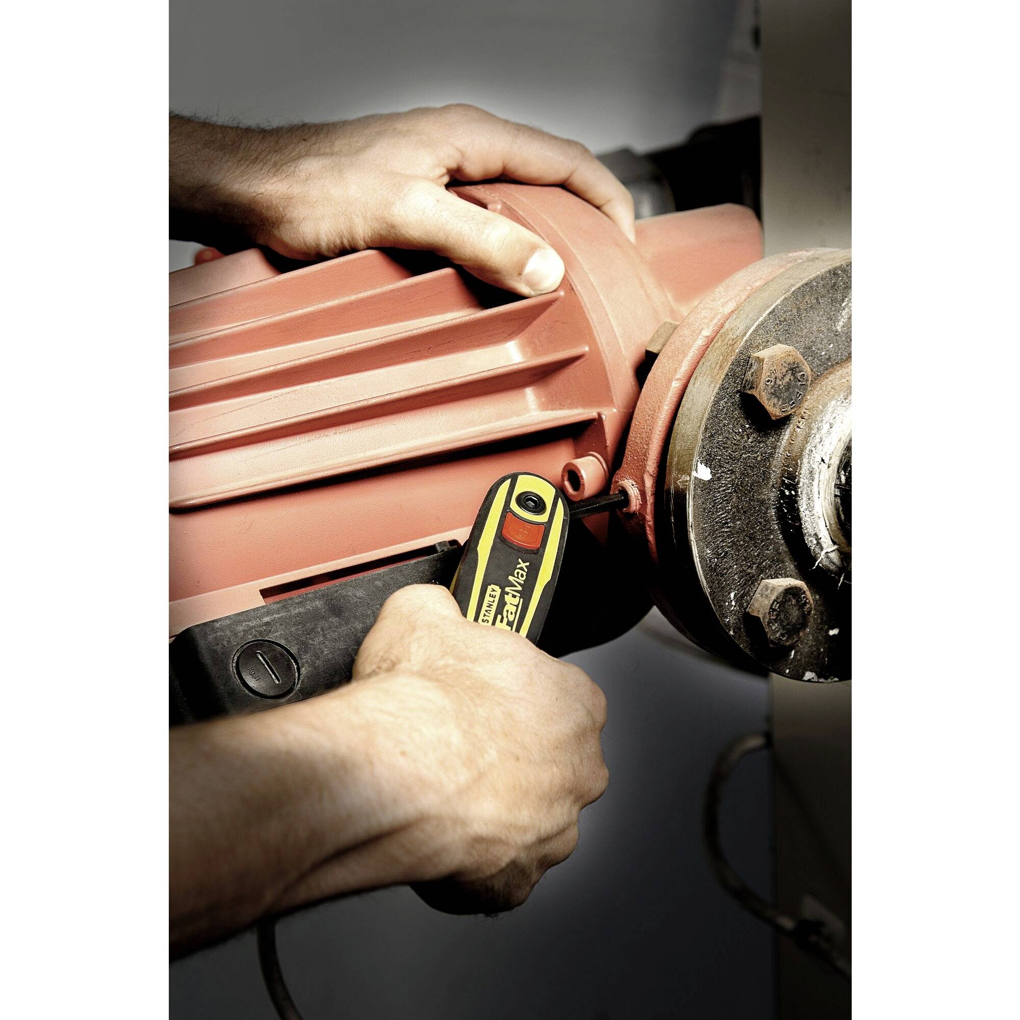 Muž používá žlutý imbus klíč k utažení šroubů velké oranžové strojové části.