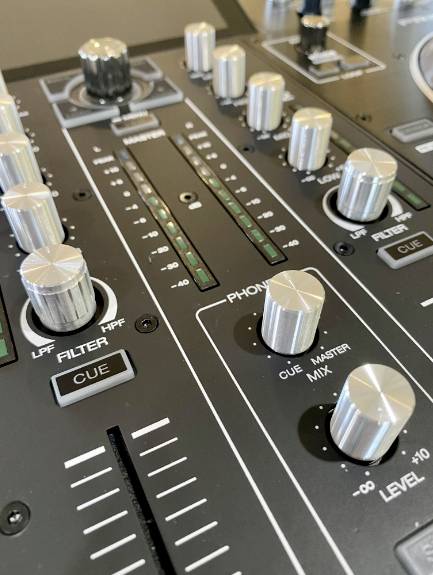 Detailní záběr mixážního pultu DJ s několika otočnými ovladači, posuvníky a tlačítky, které slouží k ovládání zvukových nastavení.