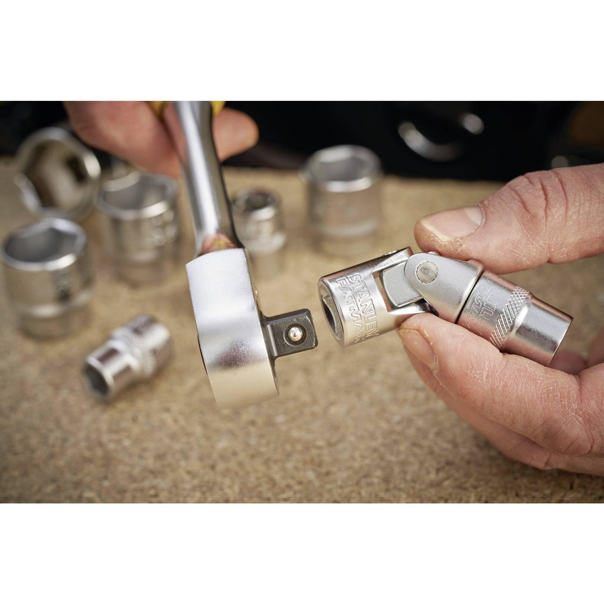 Detailní záběr rukou, které připojují ráčnu s nástavcem na nástrčný klíč. V pozadí leží další nástrčné klíče.