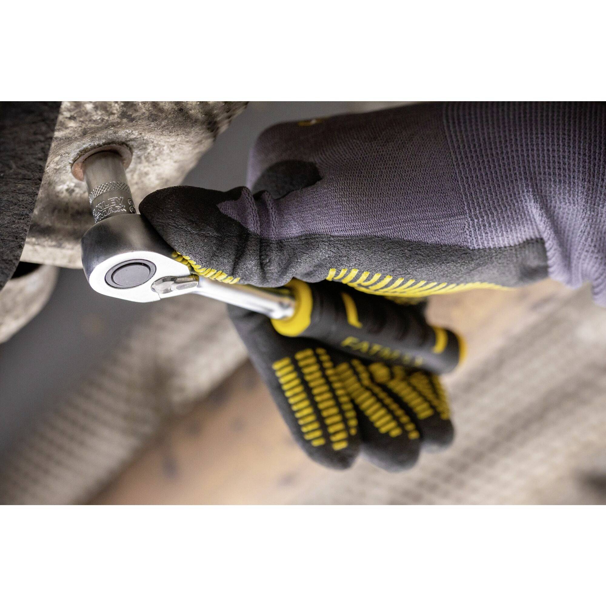 Rukavicí chráněná ruka utahuje šroub ráčnou. V pozadí je vidět kovový povrch.