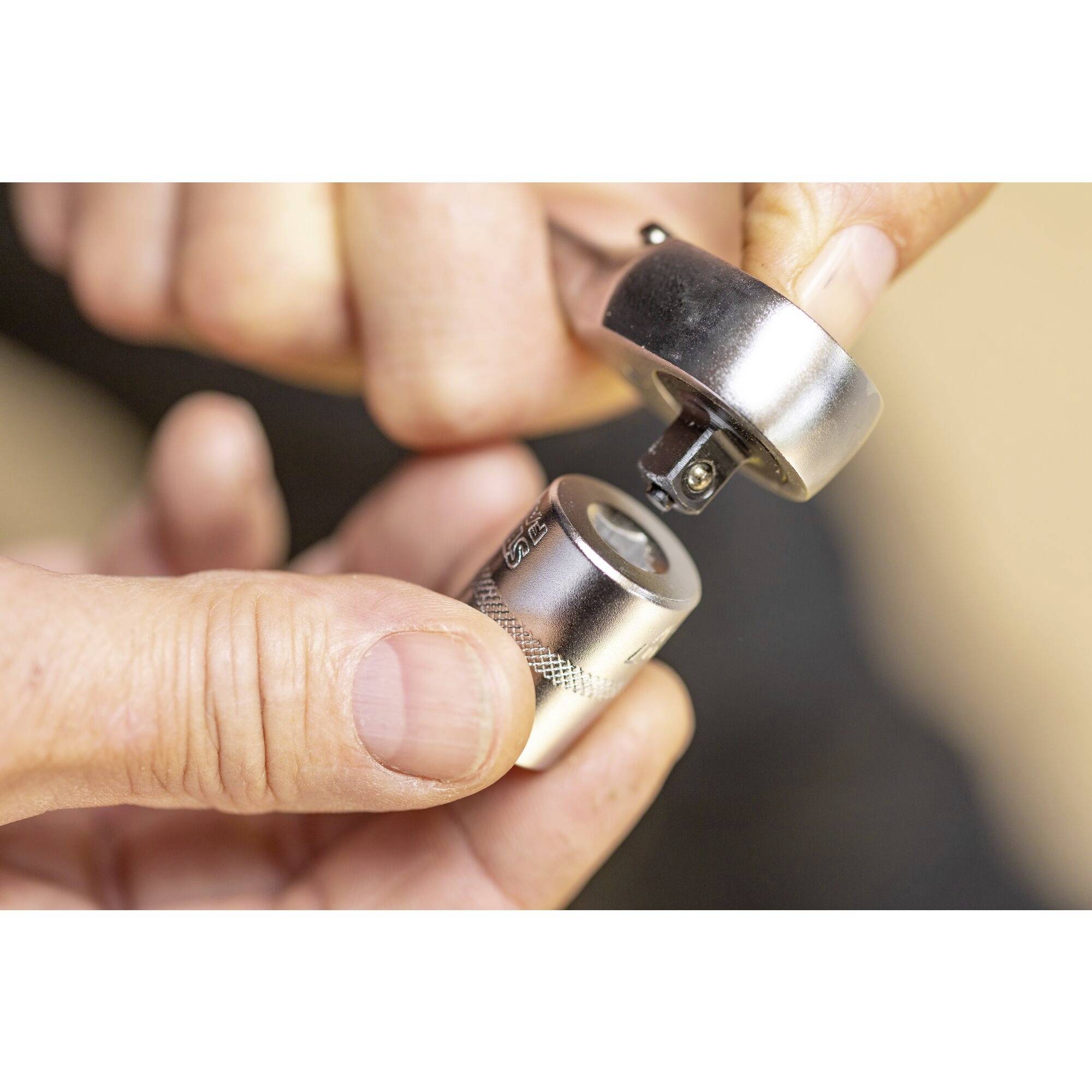 Dvě ruce drží malé válcovité kovové zařízení s odnímatelným víčkem.