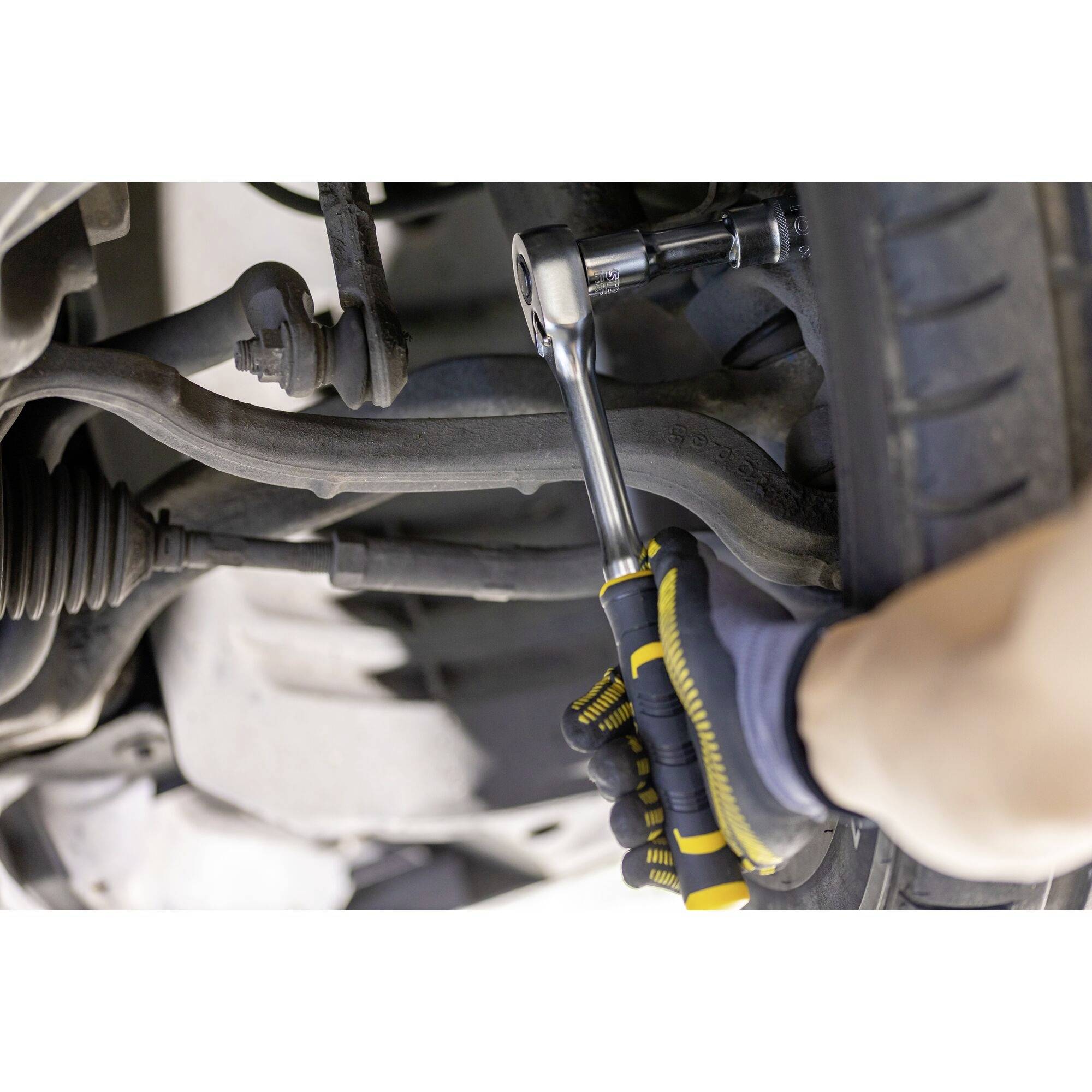 Osoba opravuje automobil, když pracuje s klíčem na zavěšení kola. Důraz je kladen na práci s nástrojem.