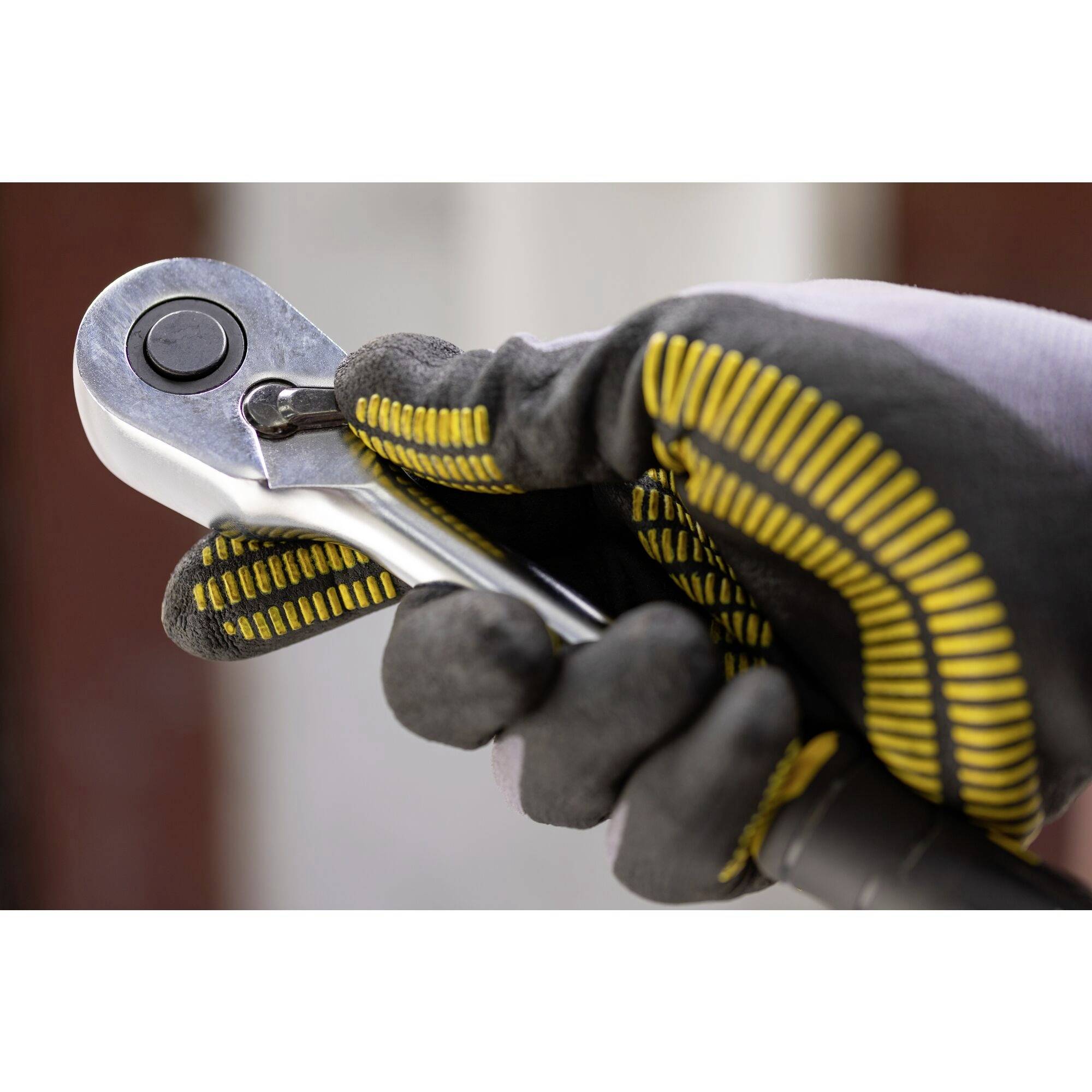 Ruka v ochranné rukavici drží ráčnový klíč.
